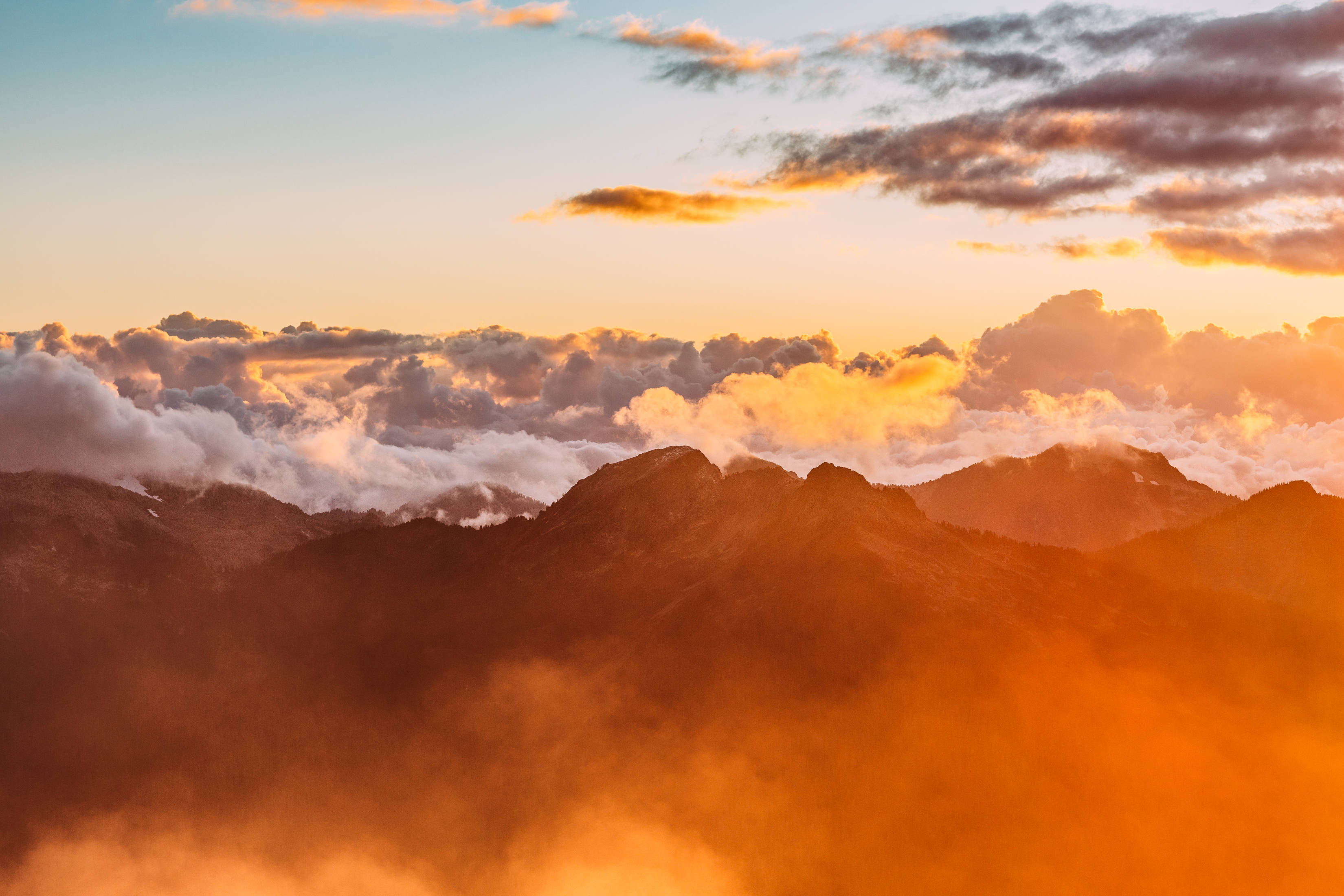 日落 桌布 壁紙 — 夕陽將山峰和雲彩染成火熱的橙色，薄霧在下方旋轉，形成戲劇性的阿爾卑斯山景。
