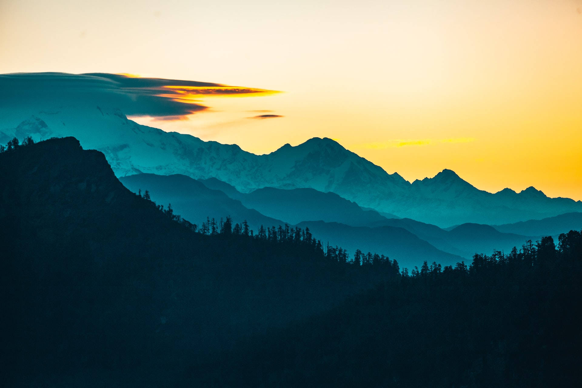 Mountain Landscape 桌布 壁紙 — 夕陽將山峰染成金橙色，層層疊疊的山脊逐漸融入清涼的藍色陰影中。