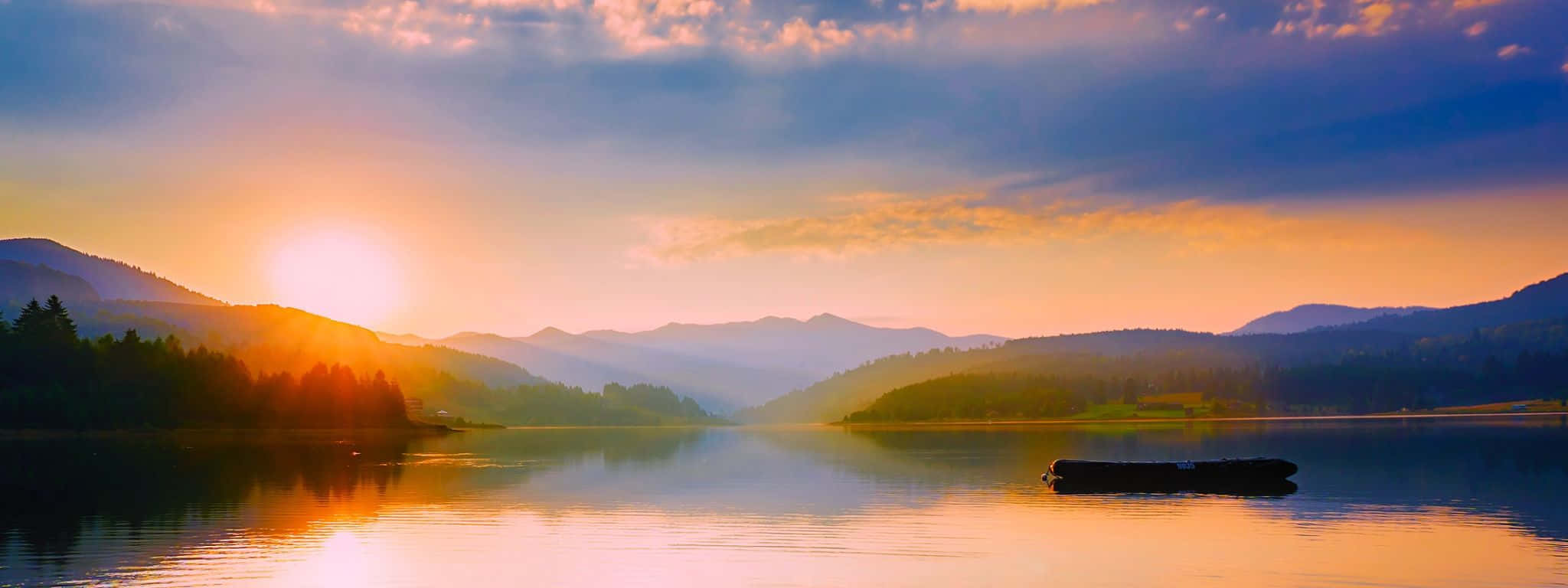 2048x768 桌布 壁紙 — 夕陽將山脈和湖泊染成溫暖的金色和深藍色，一根孤獨的木頭靜靜地漂浮在平靜的水面上。