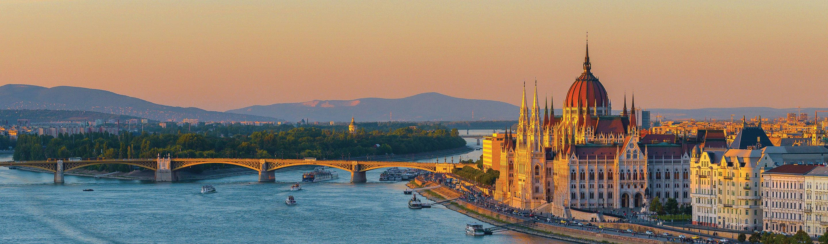 budapest 桌布 壁紙 — 夕陽將布達佩斯的國會大廈和橋樑沐浴在溫暖的金色中，多瑙河在歷史建築下流淌。