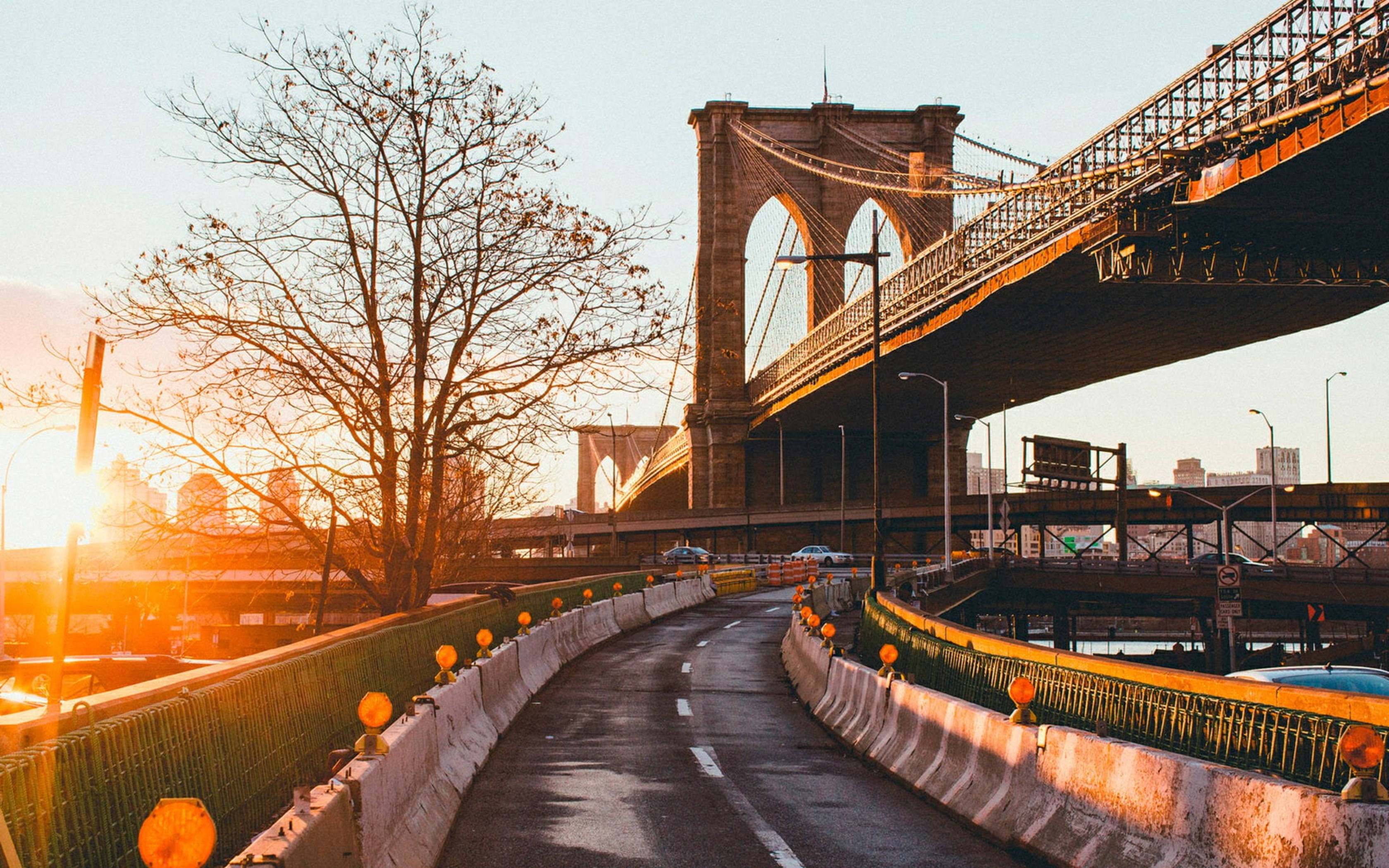 New York 桌布 壁紙 — 夕陽將布魯克林大橋沐浴在金色光芒中，蜿蜒的道路在其標誌性石拱下彎曲。
