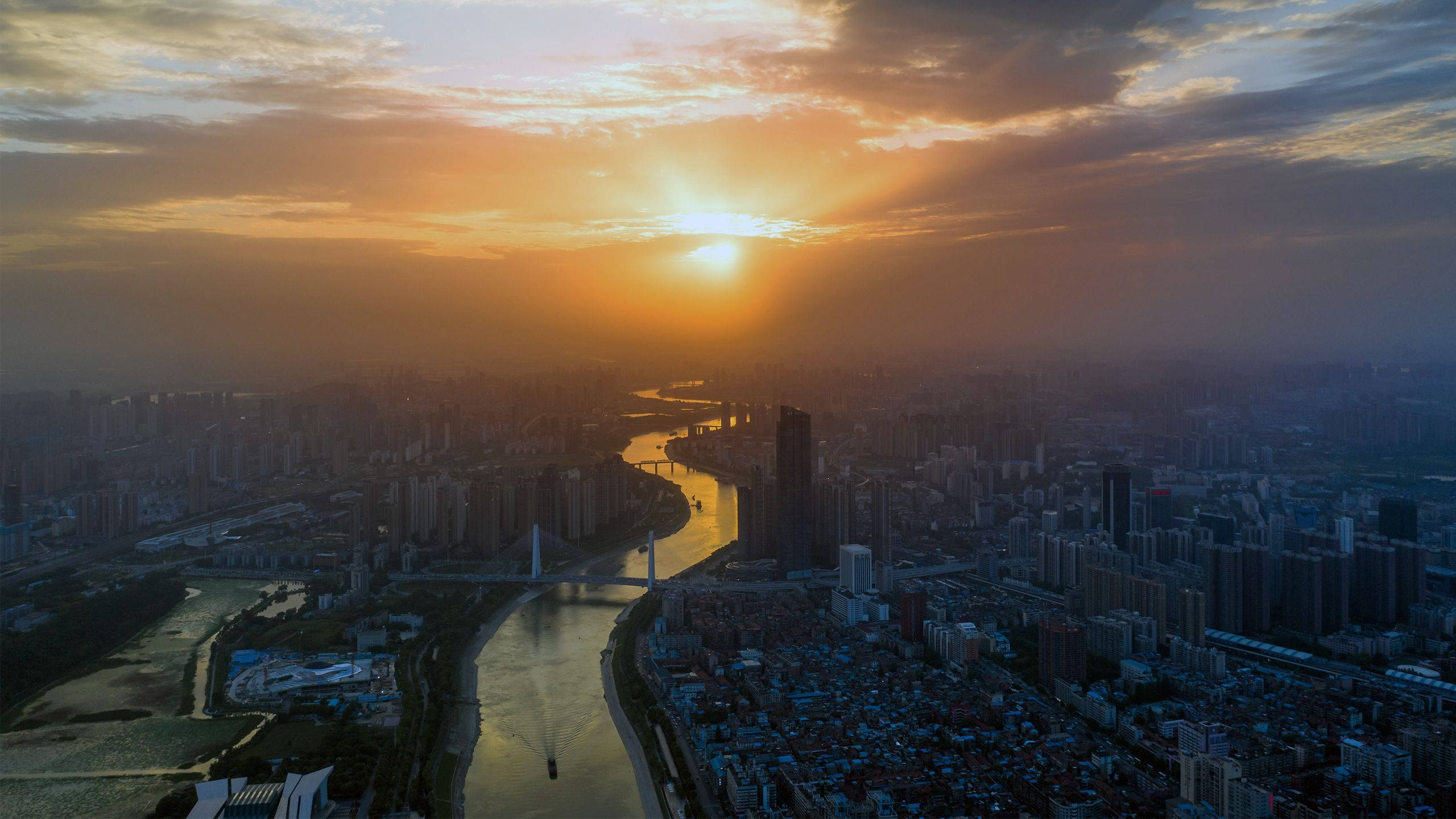 Wuhan 桌布 壁紙 — 夕陽將廣闊的城市沐浴在金色光芒中，河流蜿蜒穿過密集的摩天大樓和橋樑。