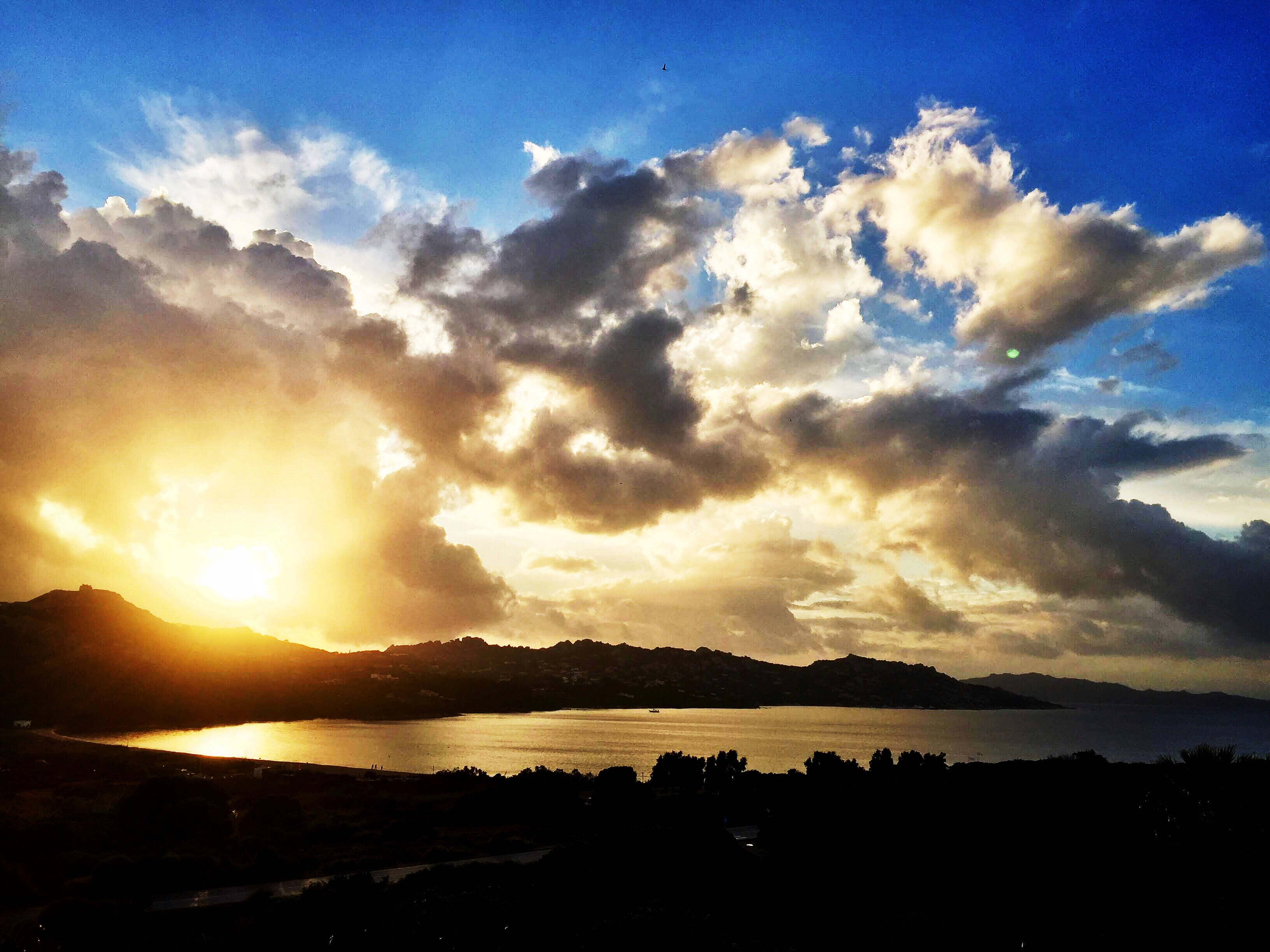 Palau 桌布 壁紙 — 夕陽將戲劇性的雲朵沐浴在金色光芒中，映照著輪廓分明的海岸灣和山丘。