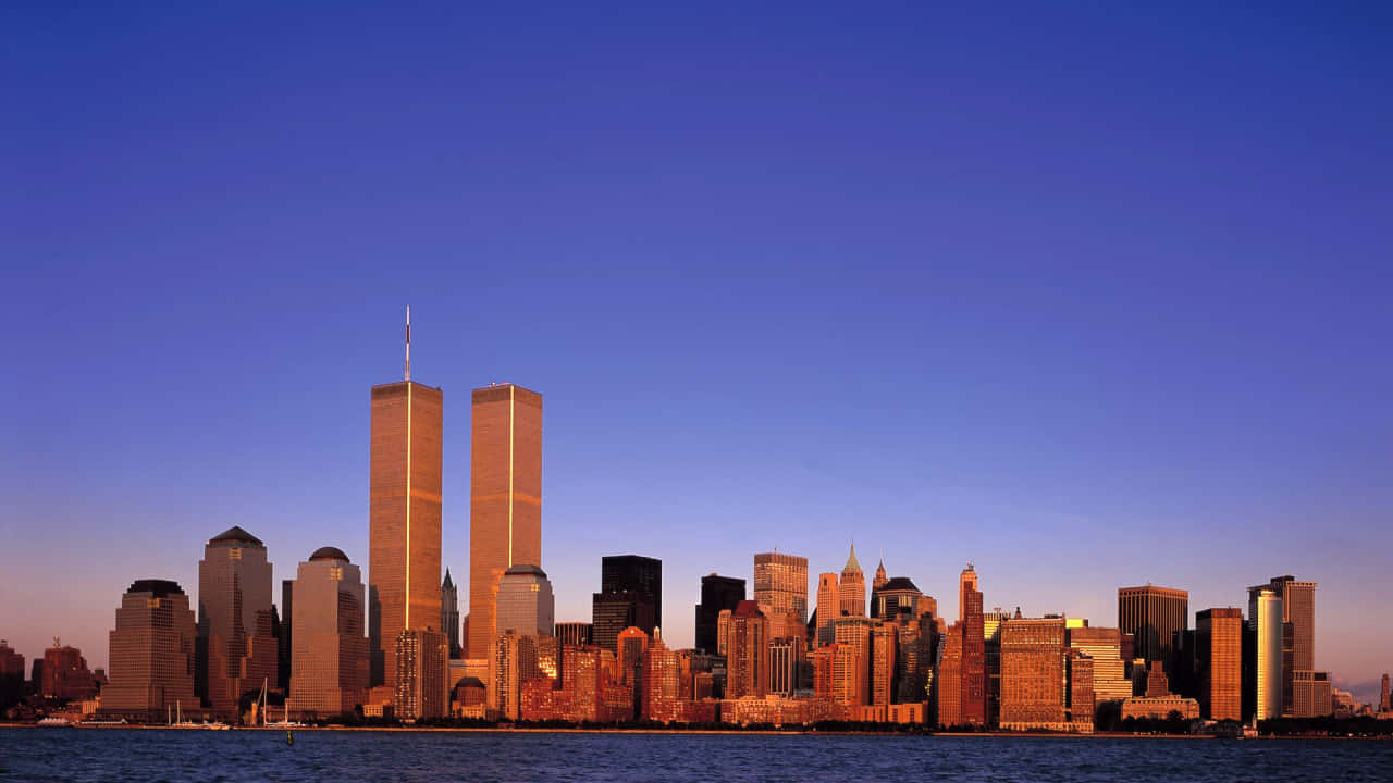 720p Ny City 桌布 壁紙 — 夕陽將標誌性的雙子塔和紐約天際線沐浴在溫暖的金色光芒中，映襯著深藍色的天空。
