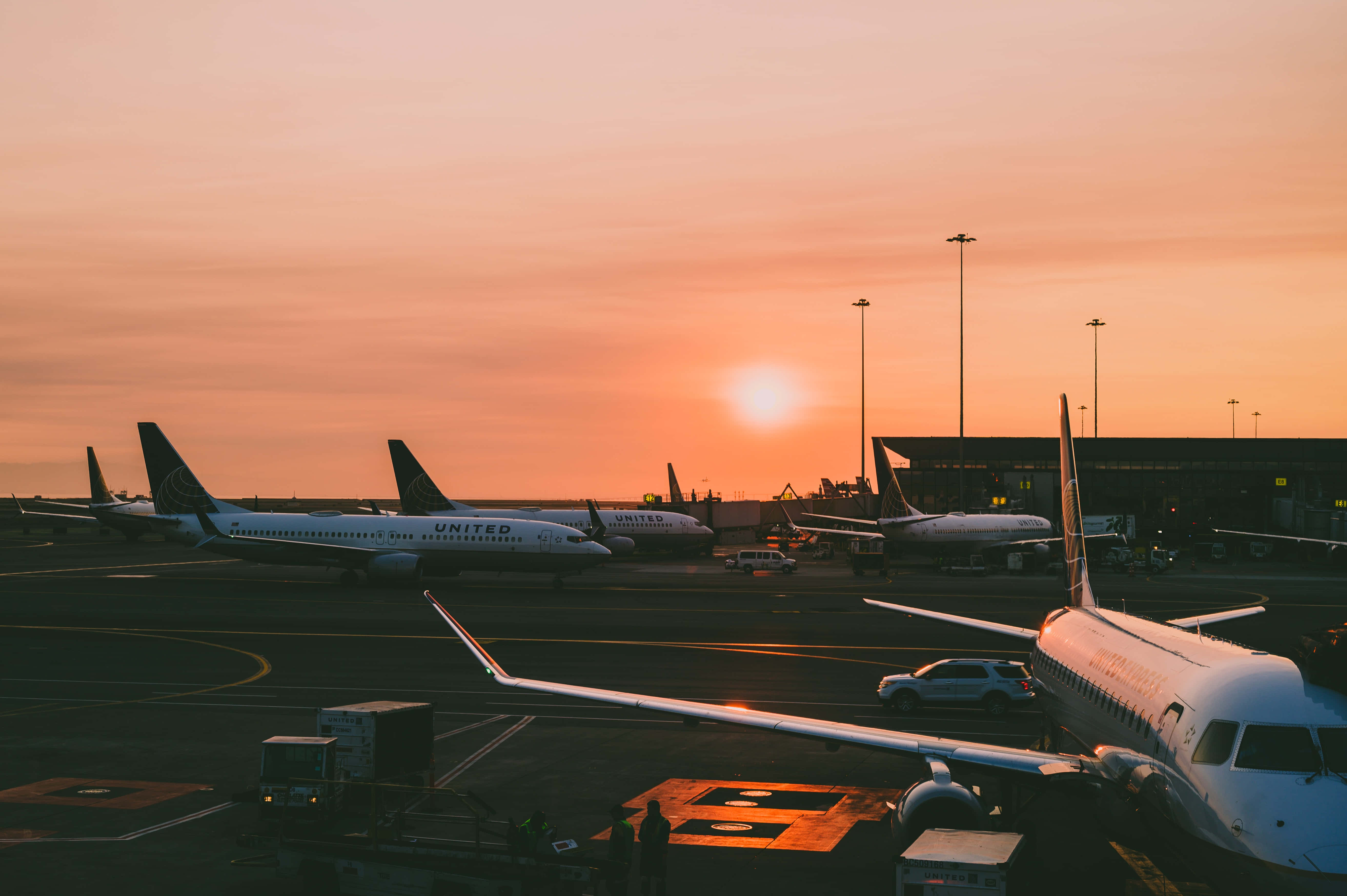 Airport 桌布 壁紙 — 夕陽將機場停機坪沐浴在溫暖的橙色光芒中，聯合航空的飛機停泊著，地勤人員和車輛呈現剪影。
