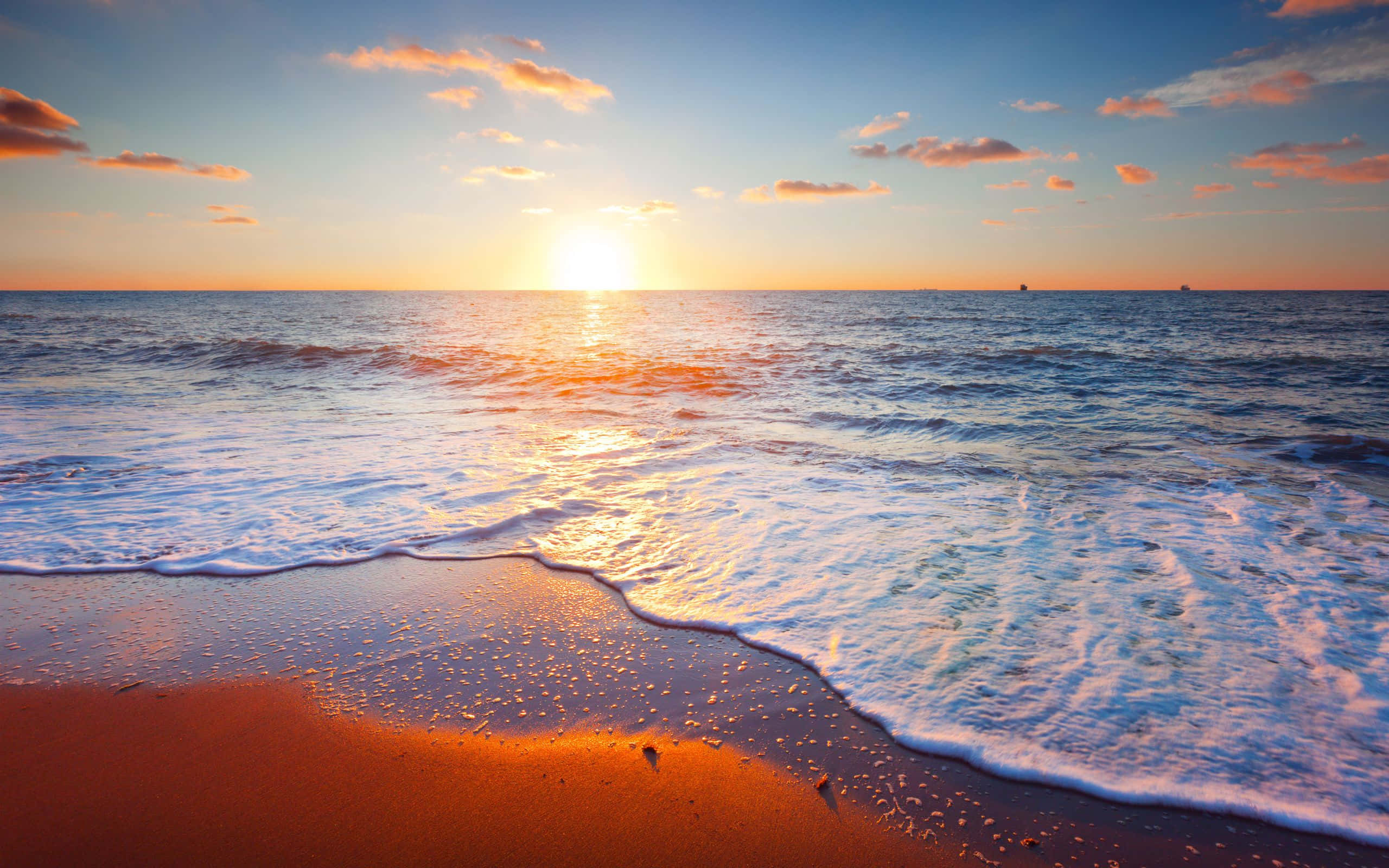 Beach Scene 桌布 壁紙 — 夕陽將海洋和沙灘染成溫暖的金色和橙色，溫柔的海浪拍打著海岸。