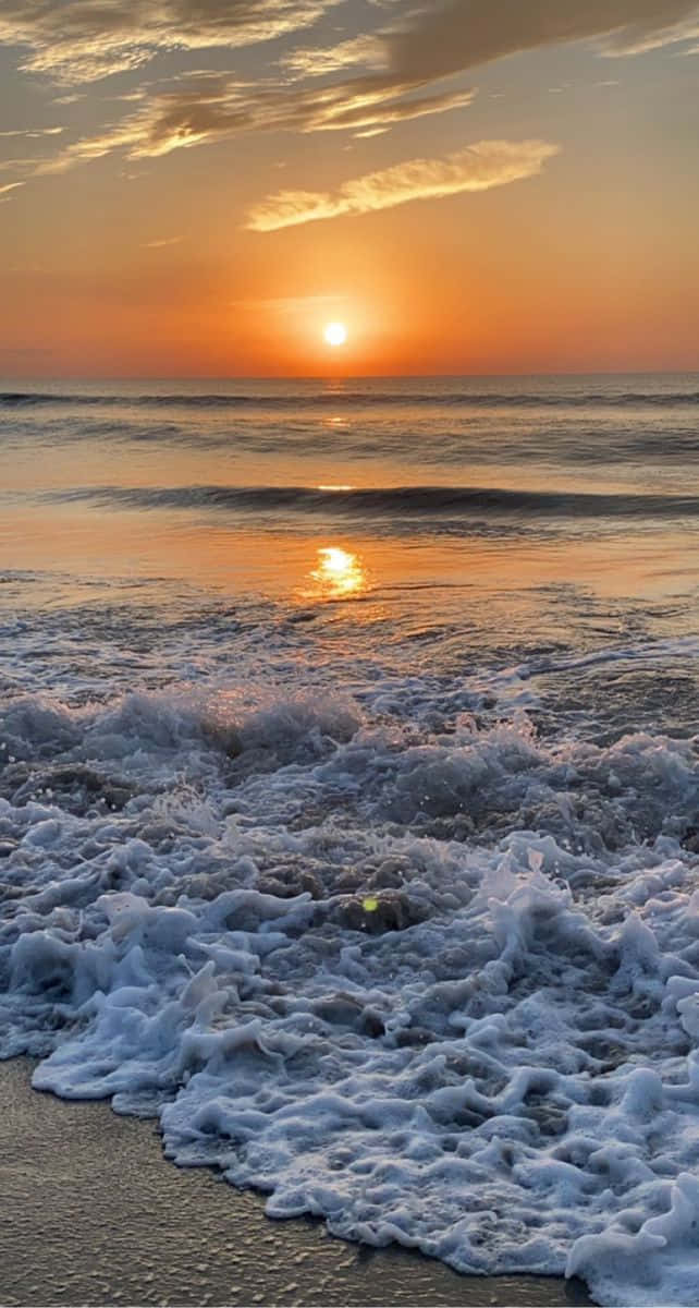 自然 桌布 壁紙 — 夕陽將海洋染成溫暖的橙色，海浪拍打沙灘，泛起白色泡沫。