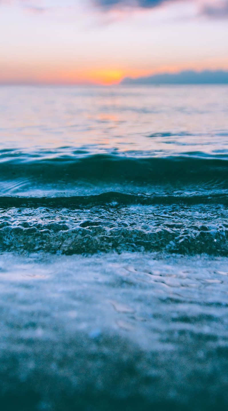 Sunset Beach iPhone 桌布 壁紙 — 夕陽將海洋染成溫暖的橙色和清涼的藍色，溫柔的海浪向岸邊翻滾。