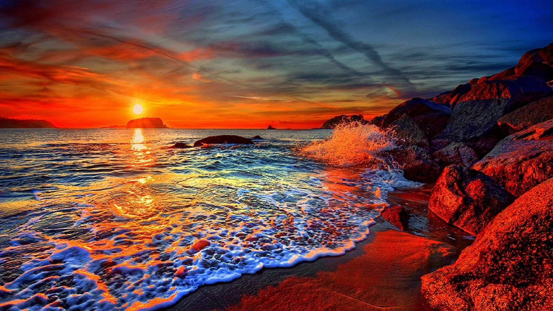 希臘 桌布 壁紙 — 夕陽將海洋染成火熱的橙色和深藍色，海浪拍打著沙灘上的崎嶇岩石。
