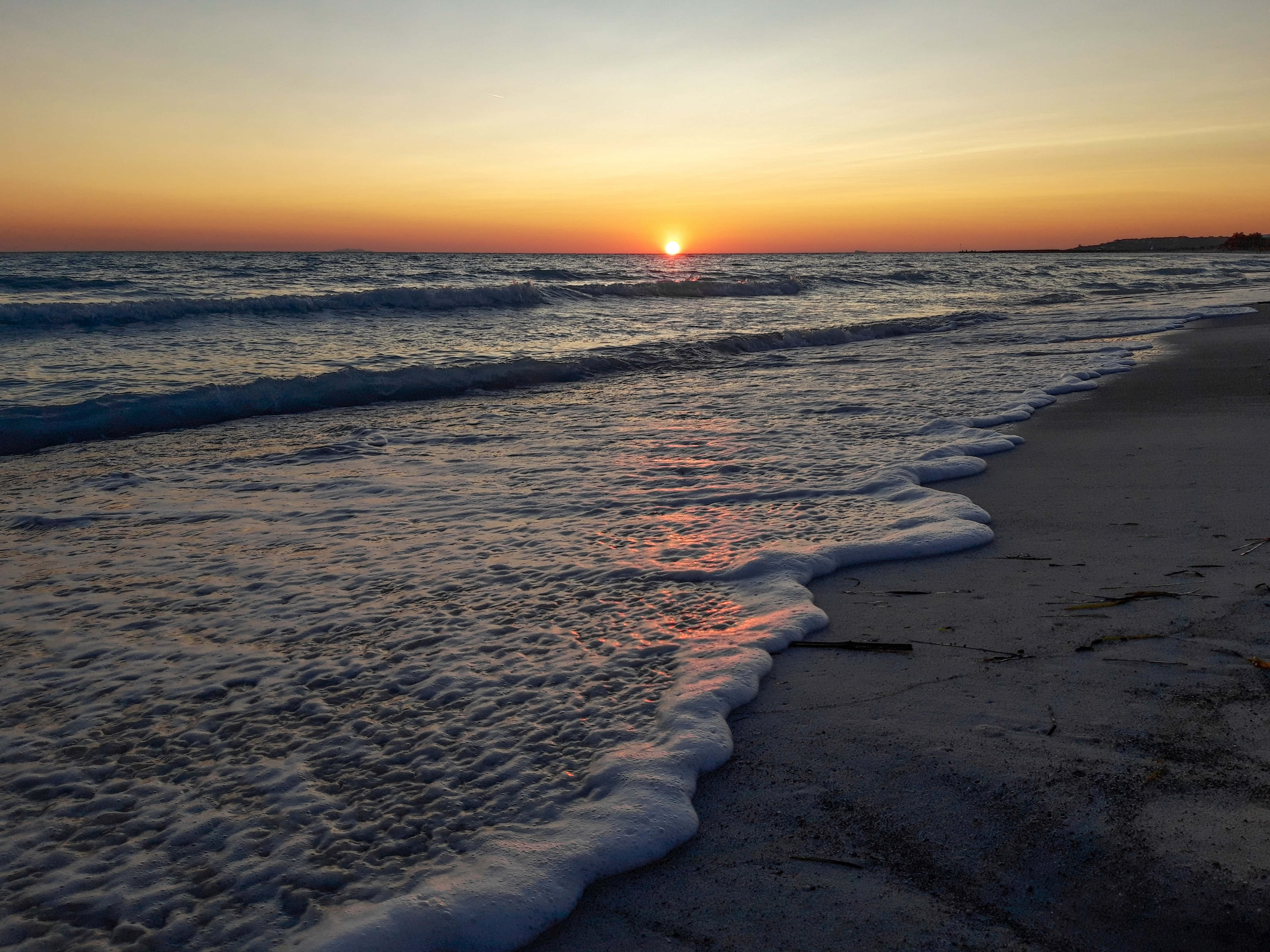 Sunset Beach 桌布 壁紙 — 夕陽將海洋染成火熱的橙色和金色，溫柔的海浪親吻著沙灘。
