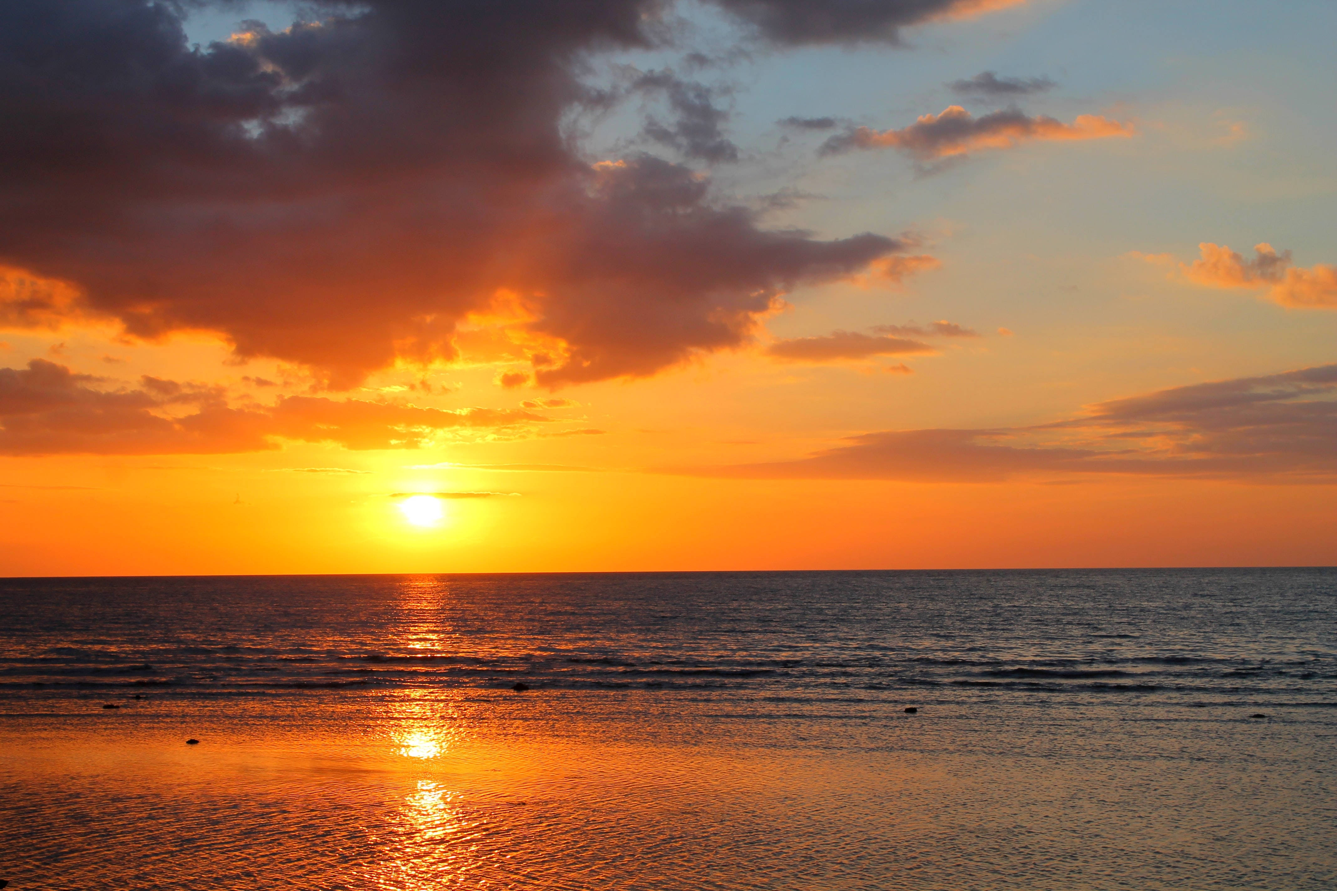 夕陽天空 桌布 壁紙 — 夕陽將海洋染成火熱的橙色和金色，太陽沉入地平線下。