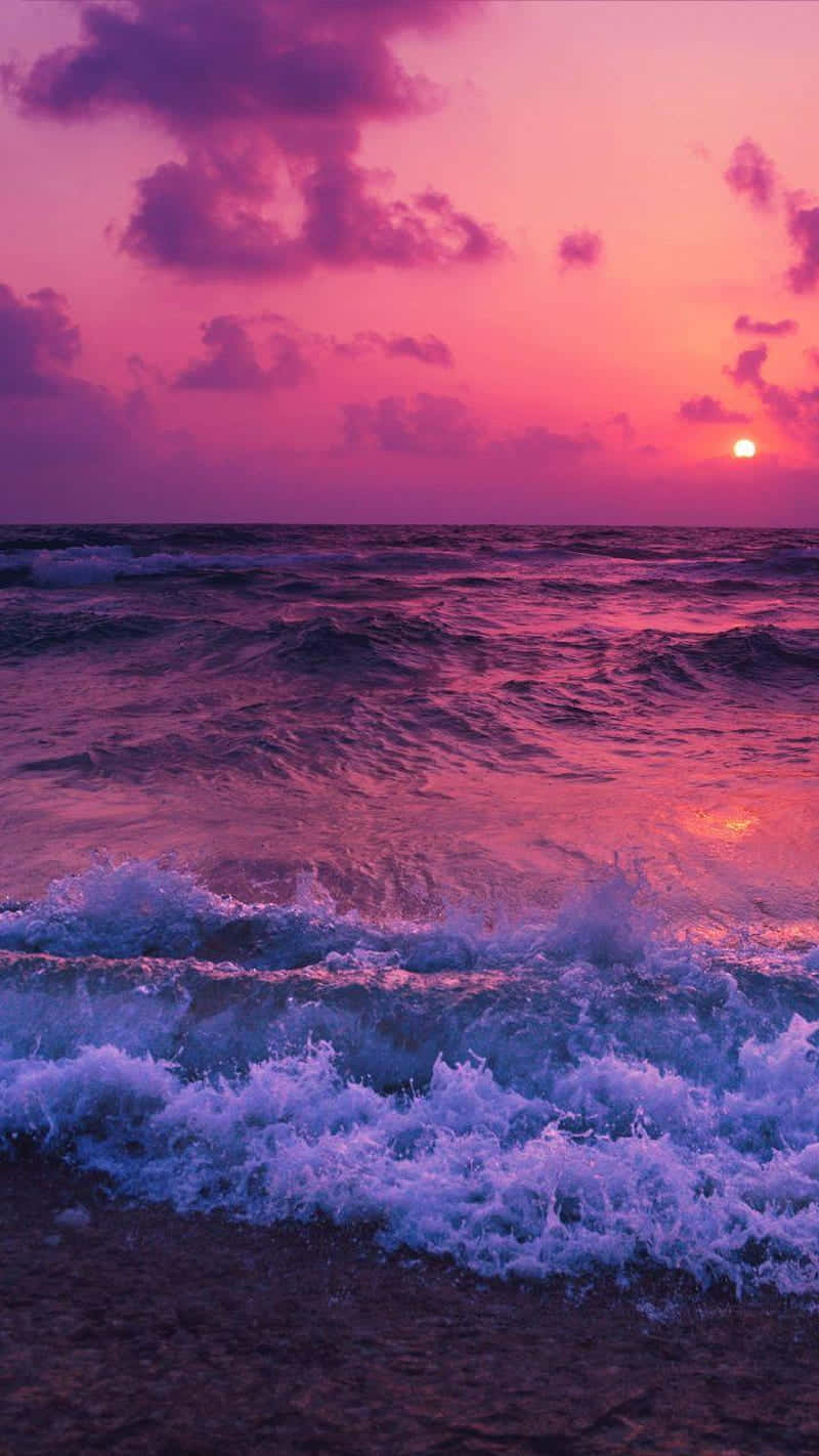 Pink Sunset iPhone 桌布 壁紙 — 夕陽將海洋染成粉紅色和紫色，海浪拍打著海岸。