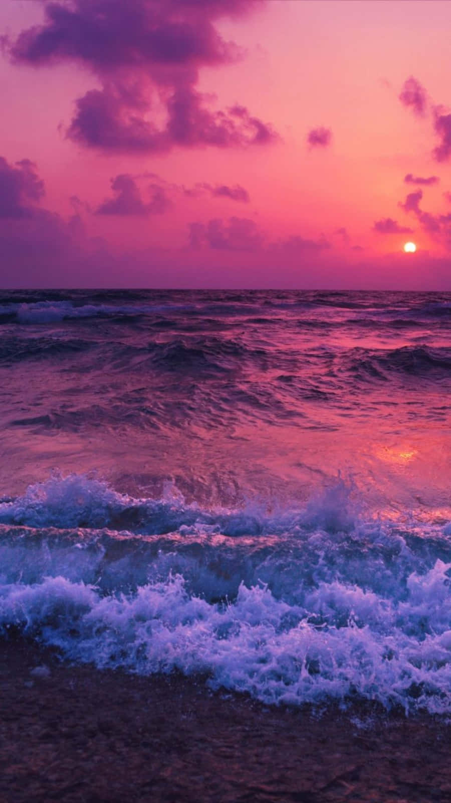 主畫面 桌布 壁紙 — 夕陽將海洋染成粉紅色和紫色，海浪拍打著海岸。