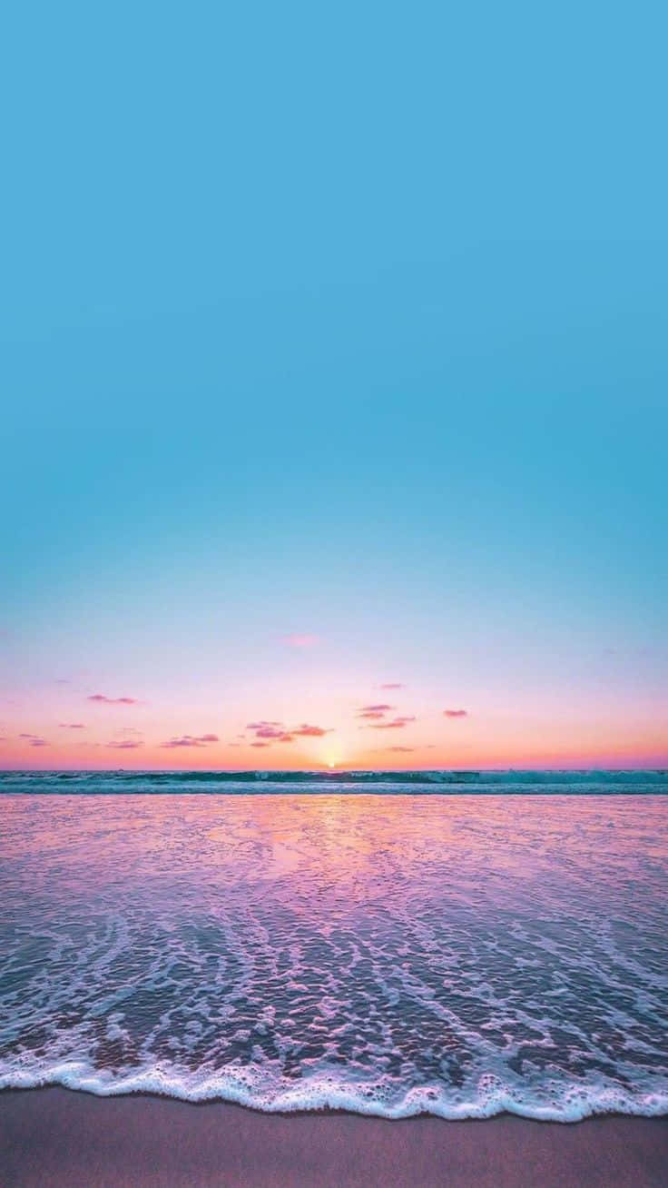 Beach Aesthetic 桌布 壁紙 — 夕陽將海洋染成粉紅色和金色，溫柔的海浪在清澈的藍天下親吻沙灘。