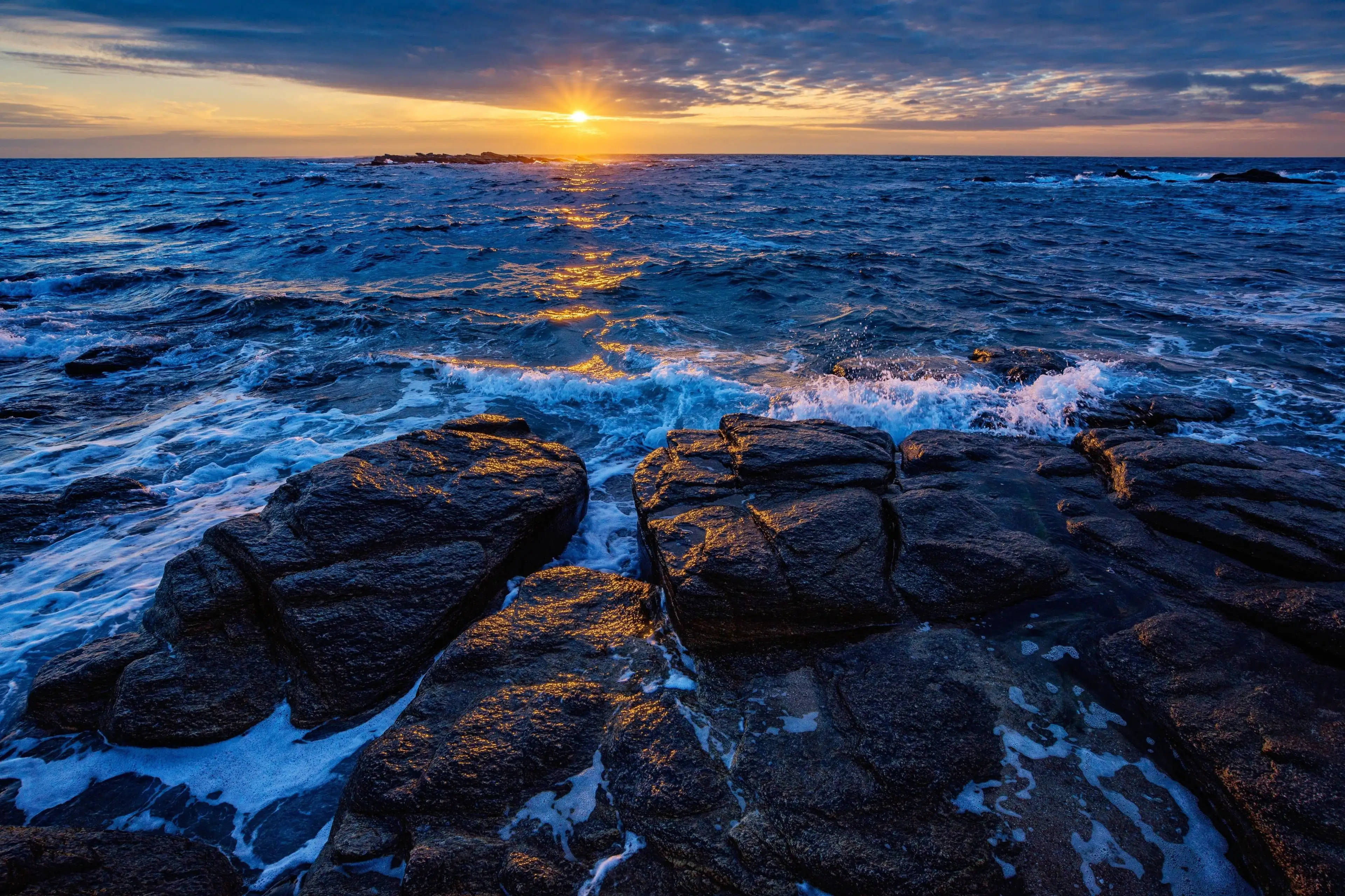 蘋果 桌布 壁紙 — 夕陽將海洋染成金色，海浪在戲劇性的天空下拍打著黑色岩石。