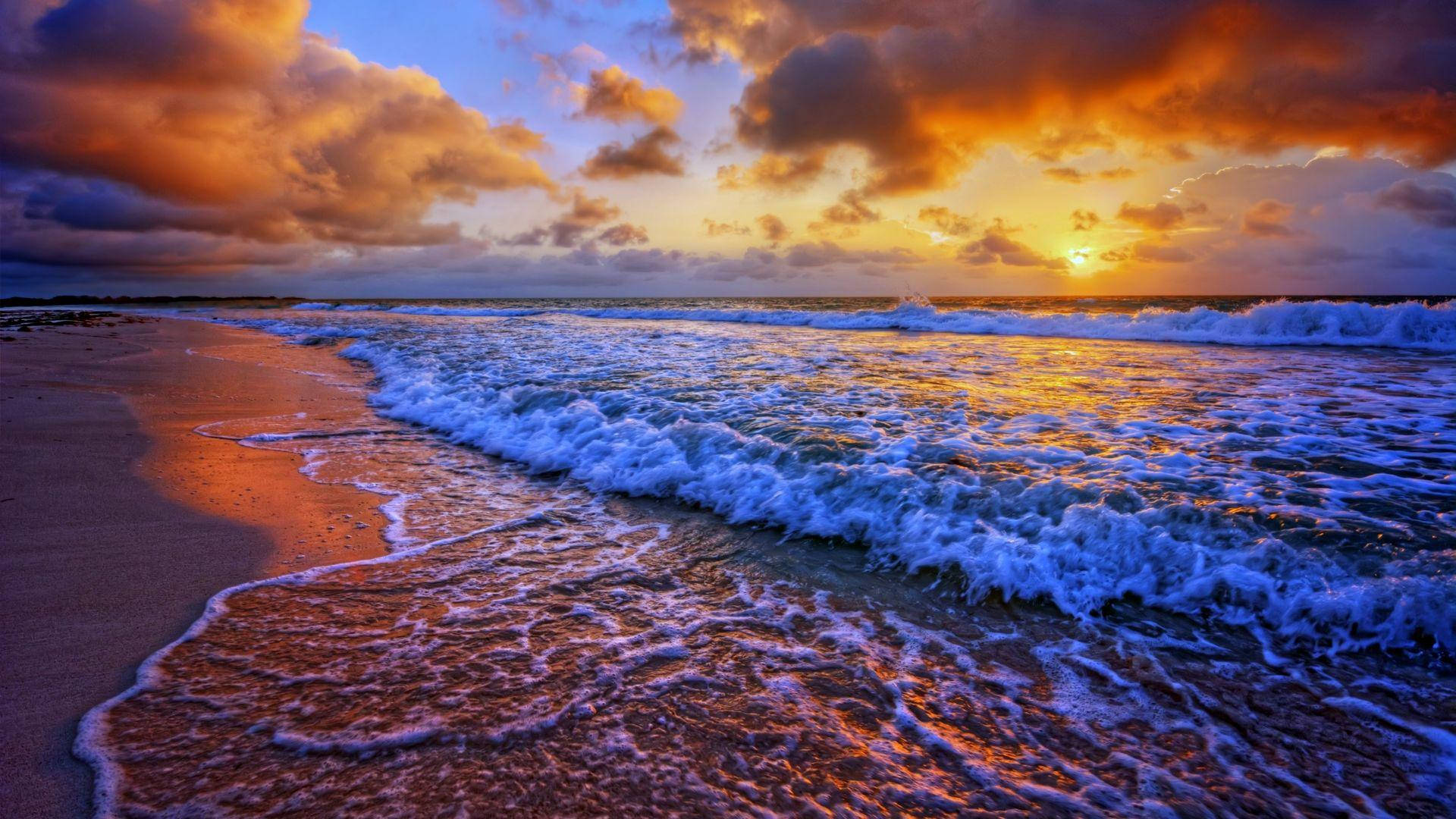 海灘日落 桌布 壁紙 — 夕陽將海浪和沙灘染成火熱的橙色和深藍色調。