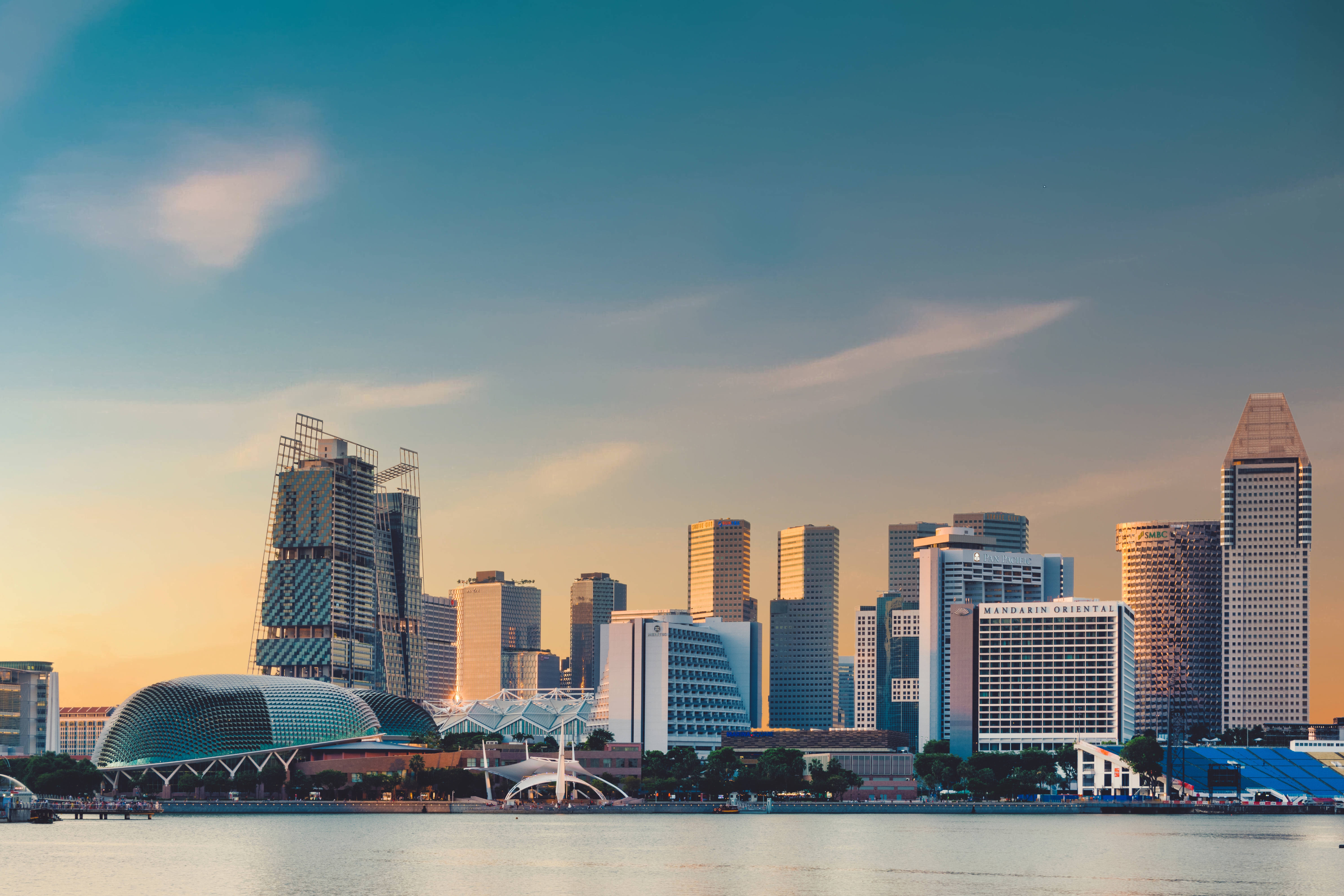 Singapore 桌布 壁紙 — 夕陽將現代新加坡的天際線沐浴在溫暖的金色光芒中，倒映在下方平靜的水面上。