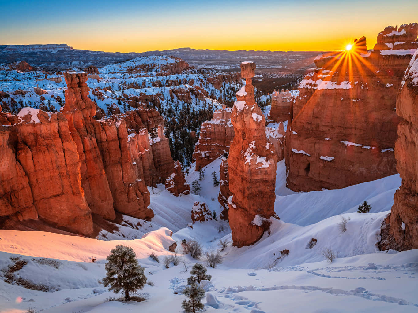 Utah 桌布 壁紙 — 夕陽將白雪覆蓋的紅色岩石尖塔沐浴在金色光芒中，橫跨廣闊的冬季峽谷。