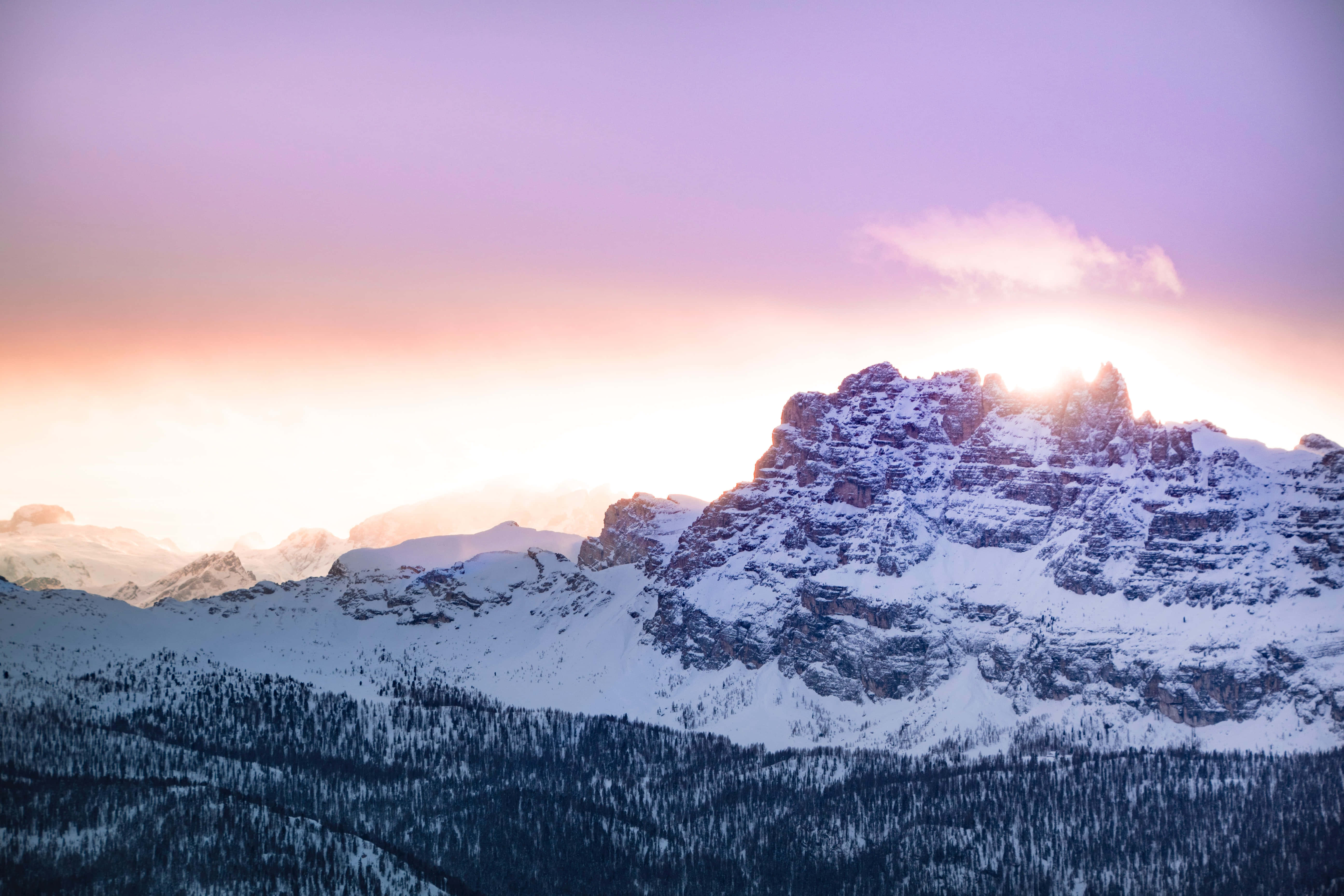 冬天 桌布 壁紙 — 夕陽將積雪的山峰染成粉紅色和紫色，光線在鋸齒狀山脊後閃耀。