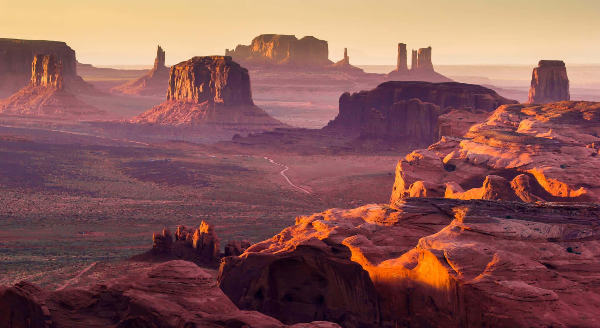 Arizona 桌布 壁紙 — 夕陽將紀念碑谷標誌性的紅色砂岩但丁沐浴在溫暖的金色光芒中，在沙漠地面上投下長長的陰影。