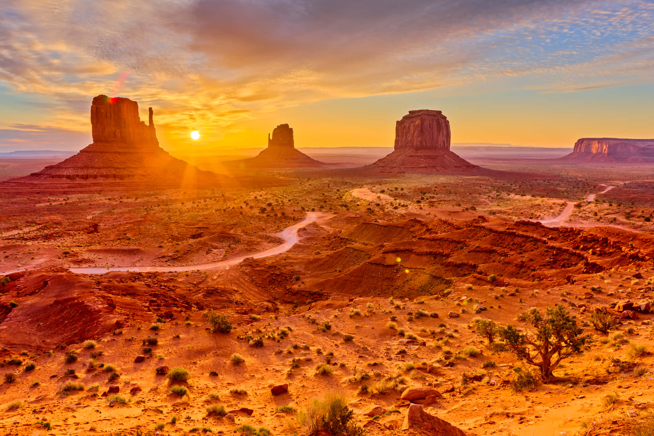 Arizona 桌布 壁紙 — 夕陽將紀念碑谷標誌性的紅色砂岩但丁山沐浴在金黃色的光芒中，在沙漠地面上投下長長的陰影。