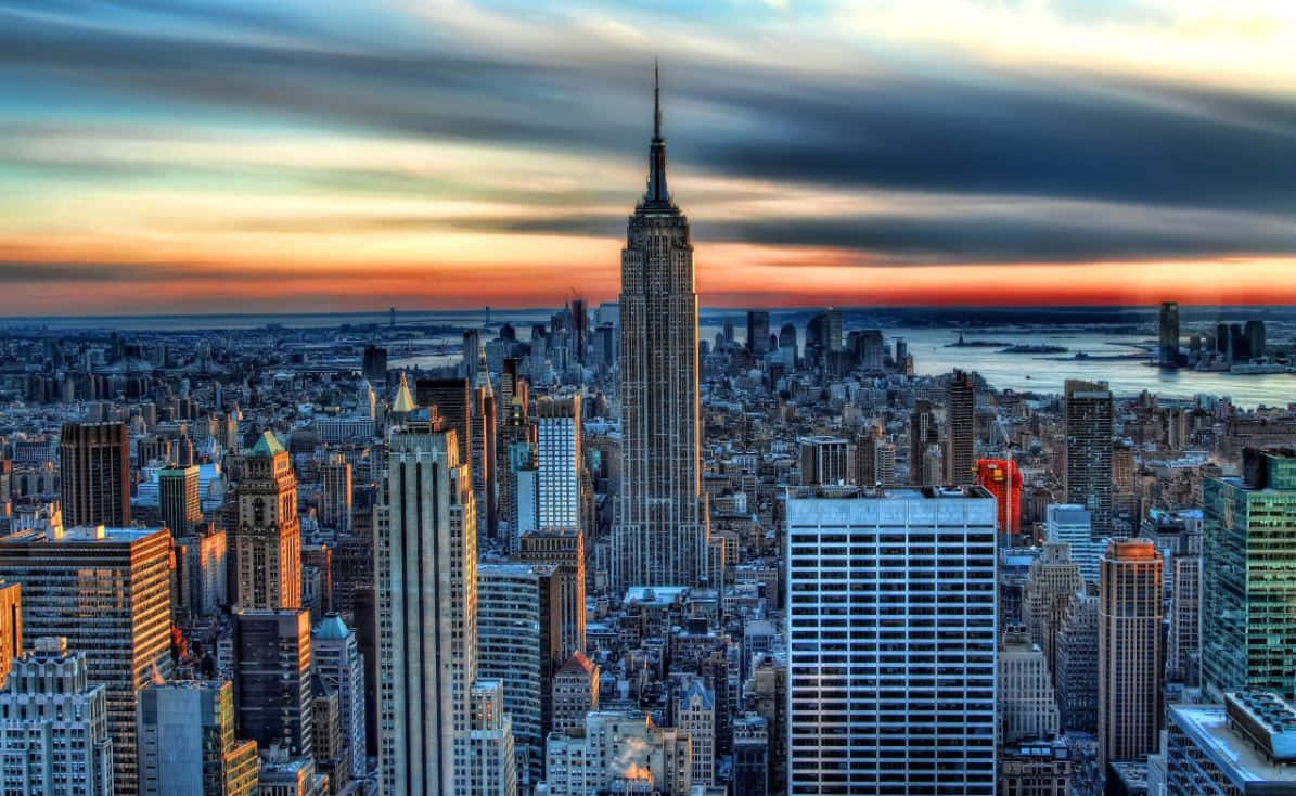 Buildings 桌布 壁紙 — 夕陽將紐約天際線染成溫暖的橙色和清涼的藍色，雲彩在帝國大廈上空劃過天際。