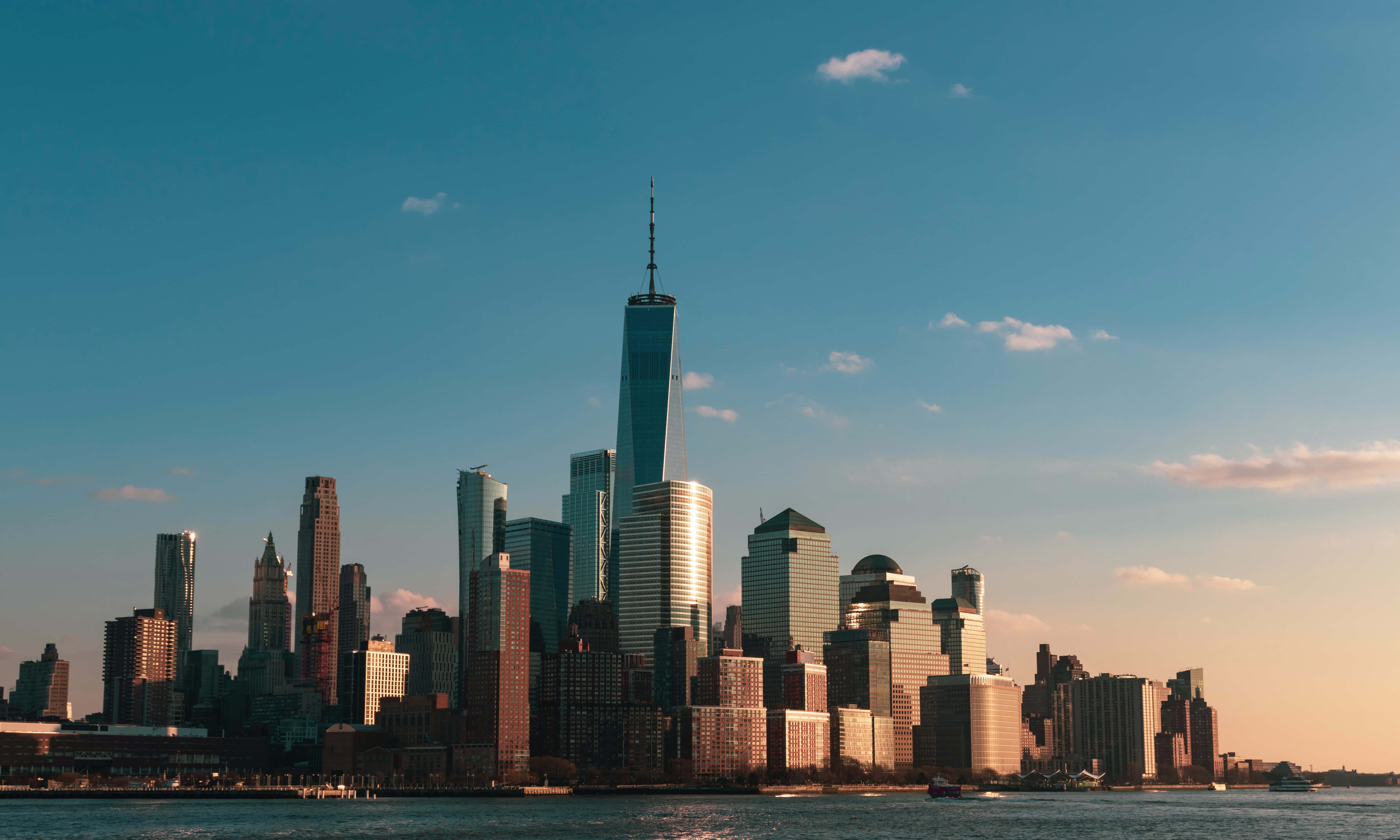 Nyc 桌布 壁紙 — 夕陽將紐約市標誌性的天際線沐浴在溫暖的金色光芒中，世界貿易中心一號大樓聳立於水面之上。