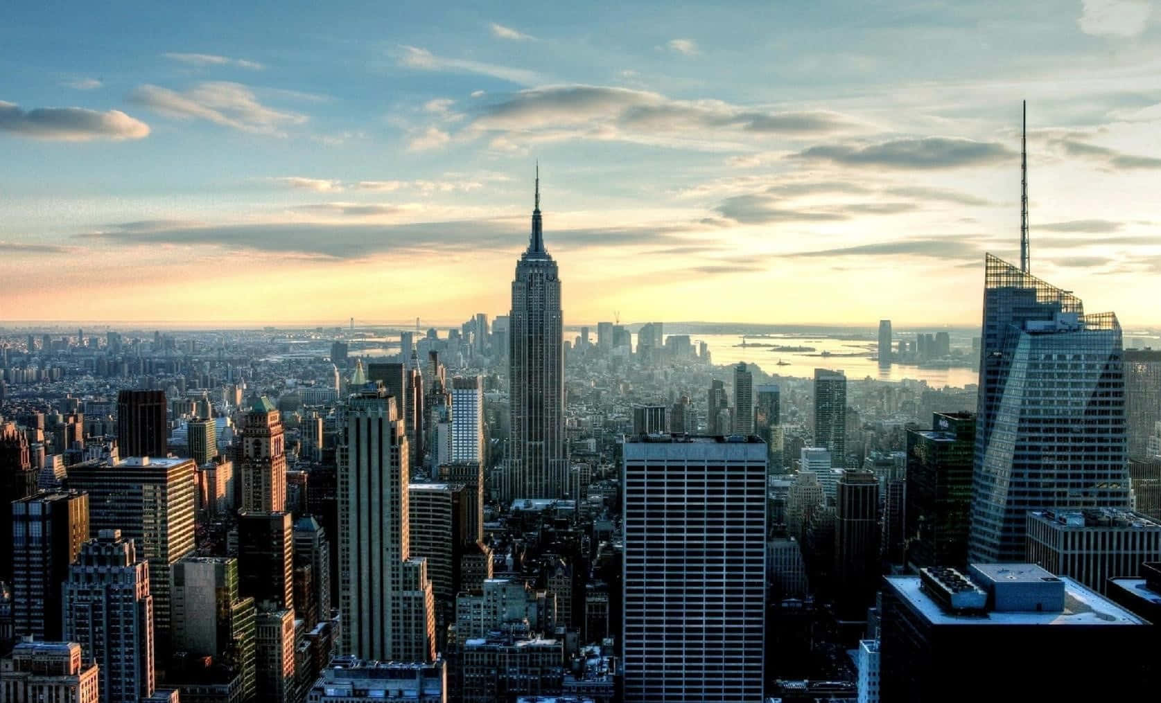 New York 桌布 壁紙 — 夕陽將紐約標誌性的天際線沐浴在金色光芒中，帝國大廈聳立在密集的城市擴展區之上。