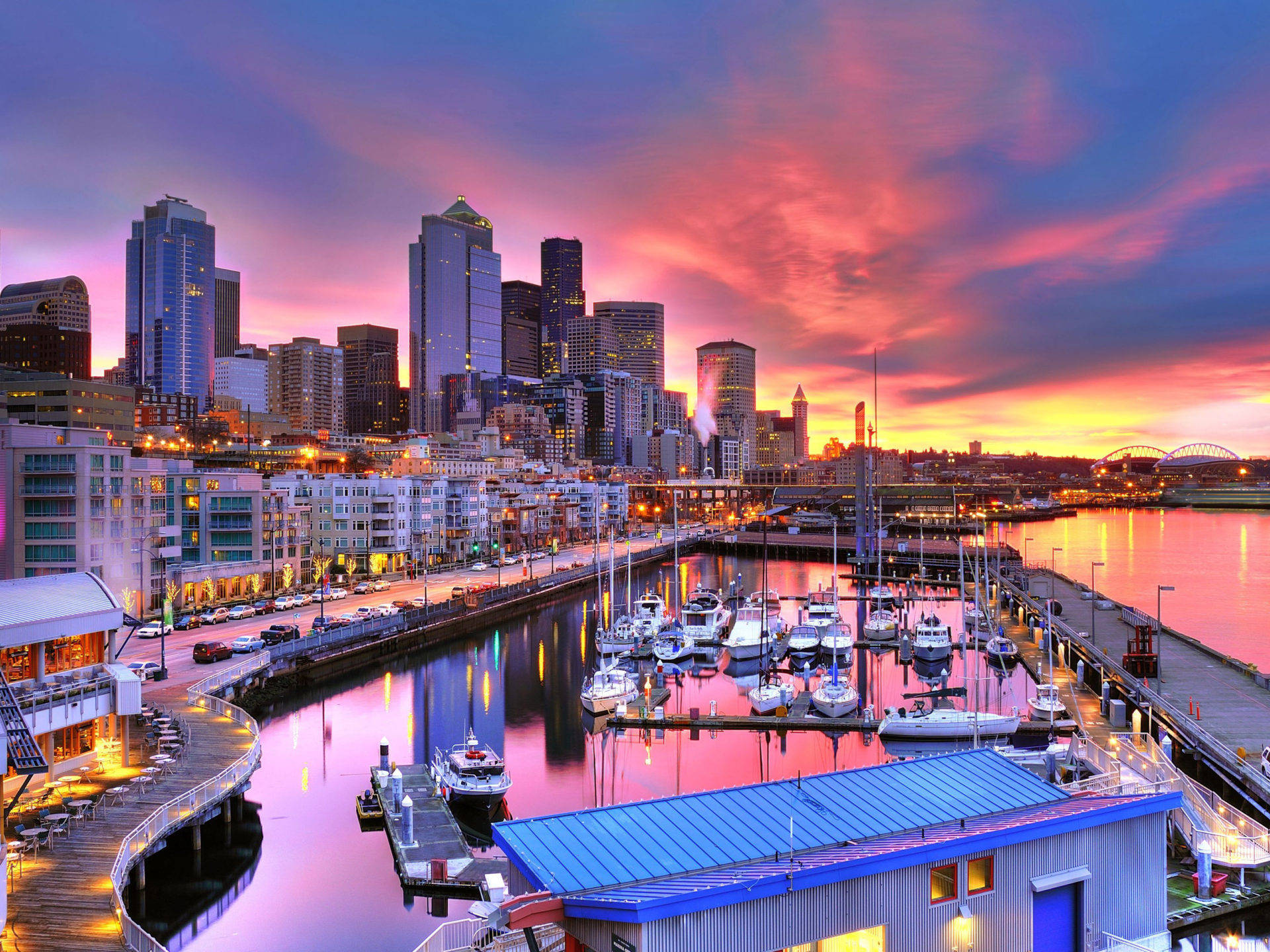 Seattle 桌布 壁紙 — 夕陽將西雅圖的天際線和港口染成火熱的粉紅色和橙色，船隻在平靜的水面上休憩。
