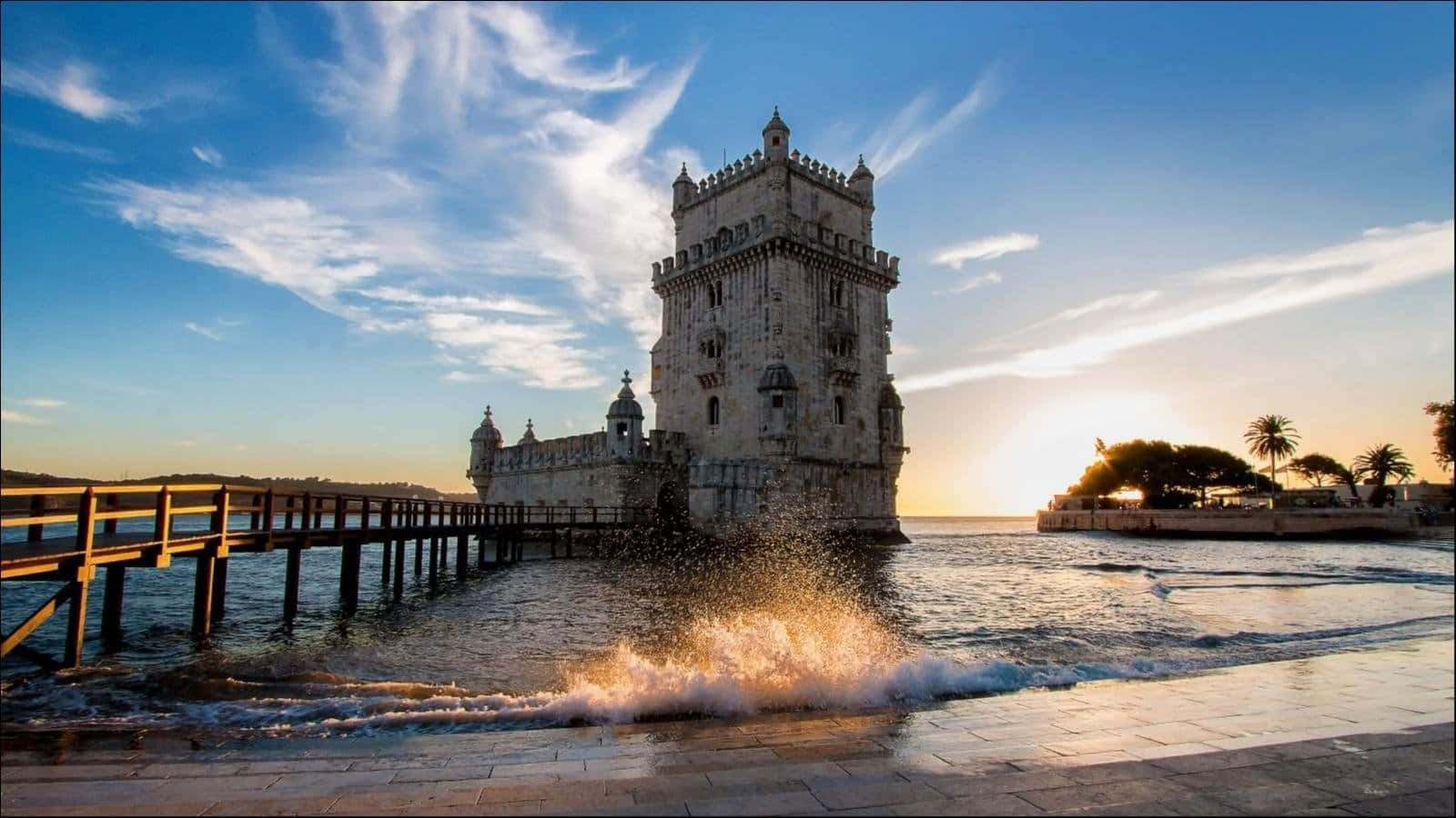 Portugal 桌布 壁紙 — 夕陽將貝倫塔沐浴在金黃色的光芒中，海浪拍打著石碼頭和瓷磚步道。