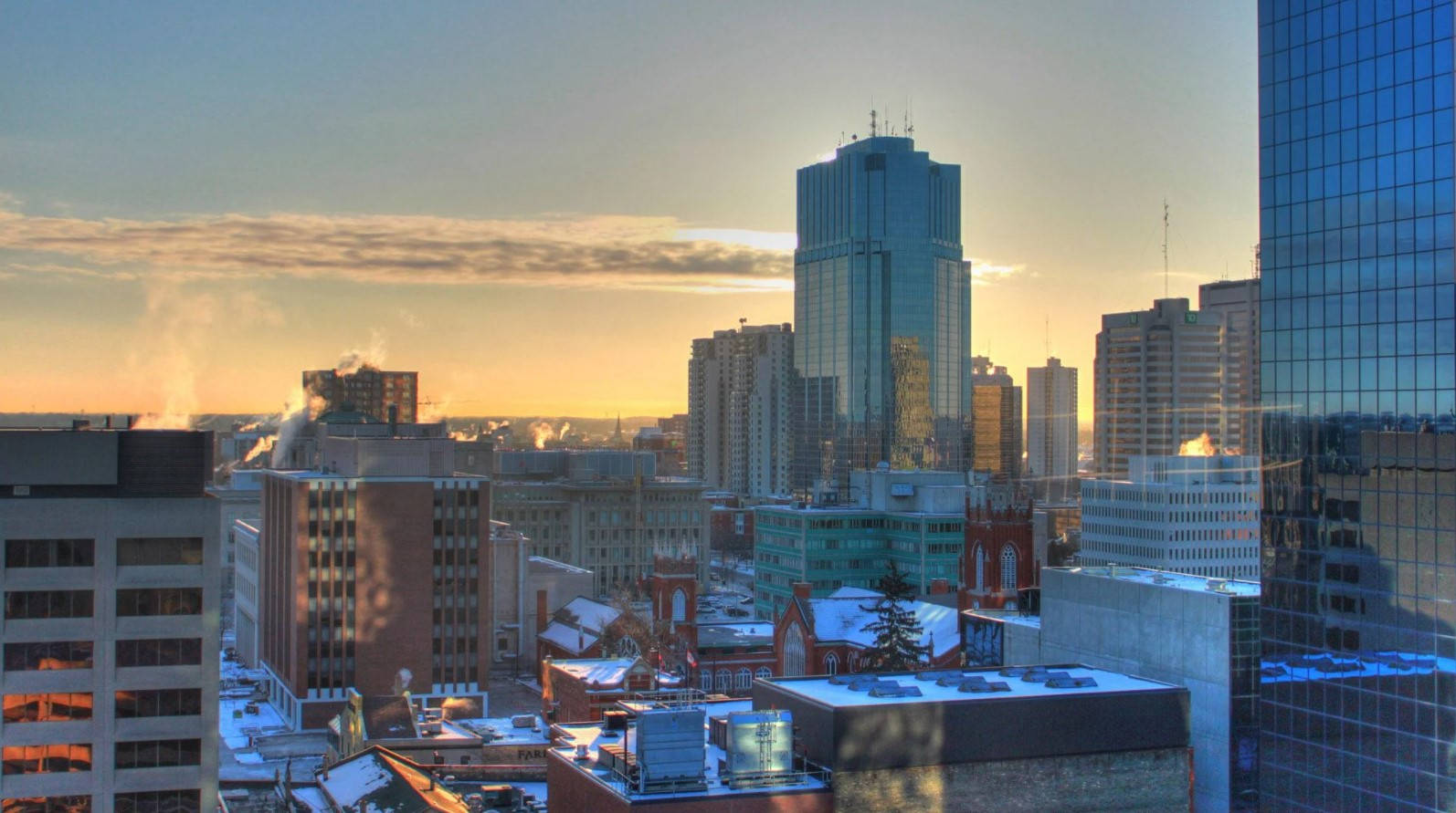 Ontario 桌布 壁紙 — 夕陽將金色光芒灑在積雪的屋頂和反射天空的玻璃摩天大樓上。