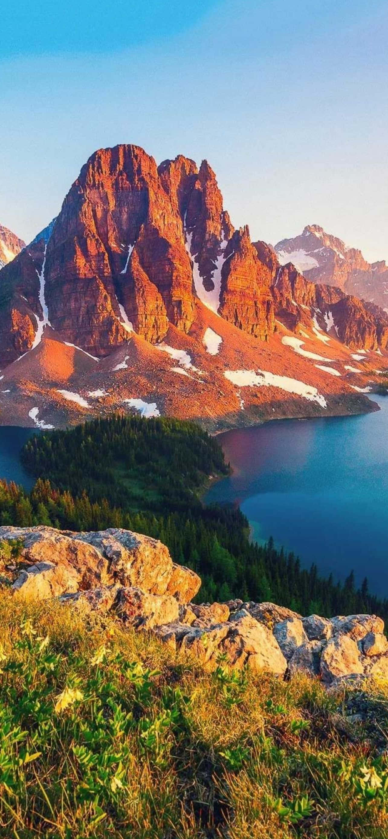 Mountain iPhone 桌布 壁紙 — 夕陽將鋸齒狀的紅色山脈和寧靜的藍色湖泊沐浴在溫暖的金色光芒中，山頂上殘留著雪斑。