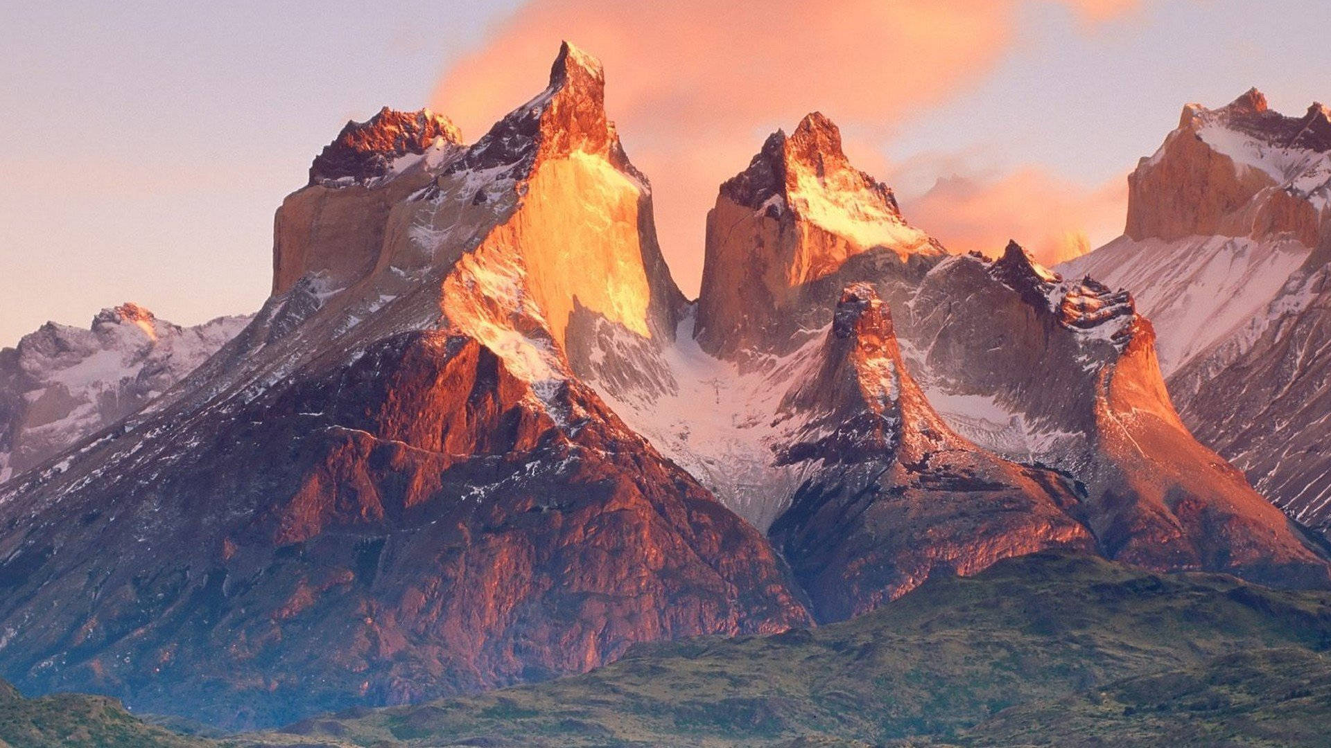 Patagonia 桌布 壁紙 — 夕陽將鋸齒狀的雪山頂峰沐浴在溫暖的金色光芒中，映襯著柔和的粉紅色天空。
