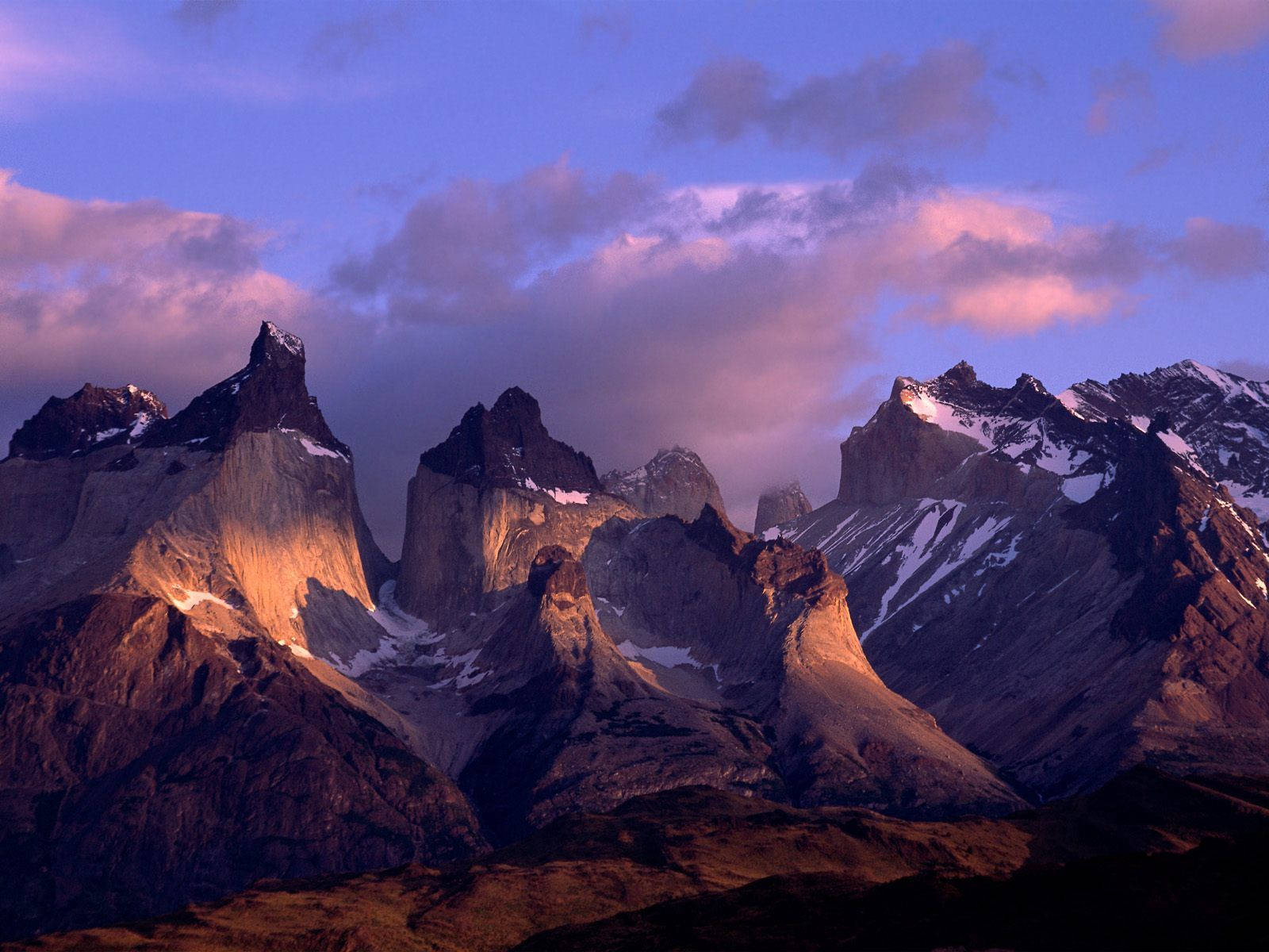 Chile 桌布 壁紙 — 夕陽將鋸齒狀的雪峰沐浴在溫暖的金色中，映襯著紫色的天空和柔和的粉紅色雲彩。