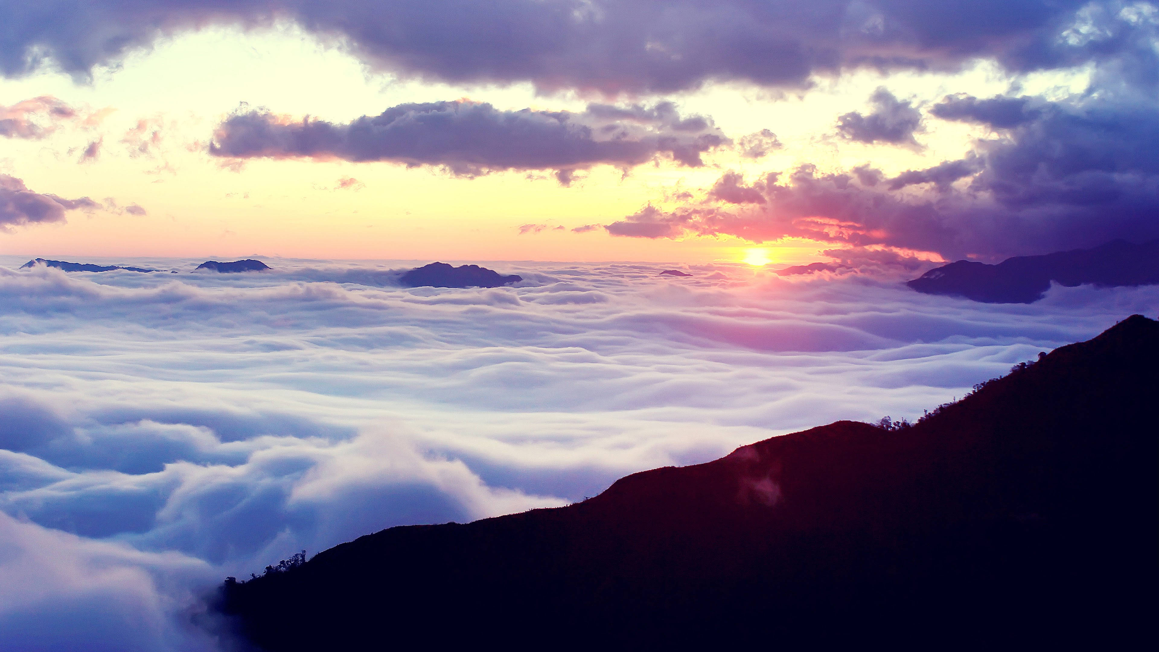 Outlook 桌布 壁紙 — 夕陽將雲彩染成火熱的橙色和紫色，山脈在雲海之上聳立。
