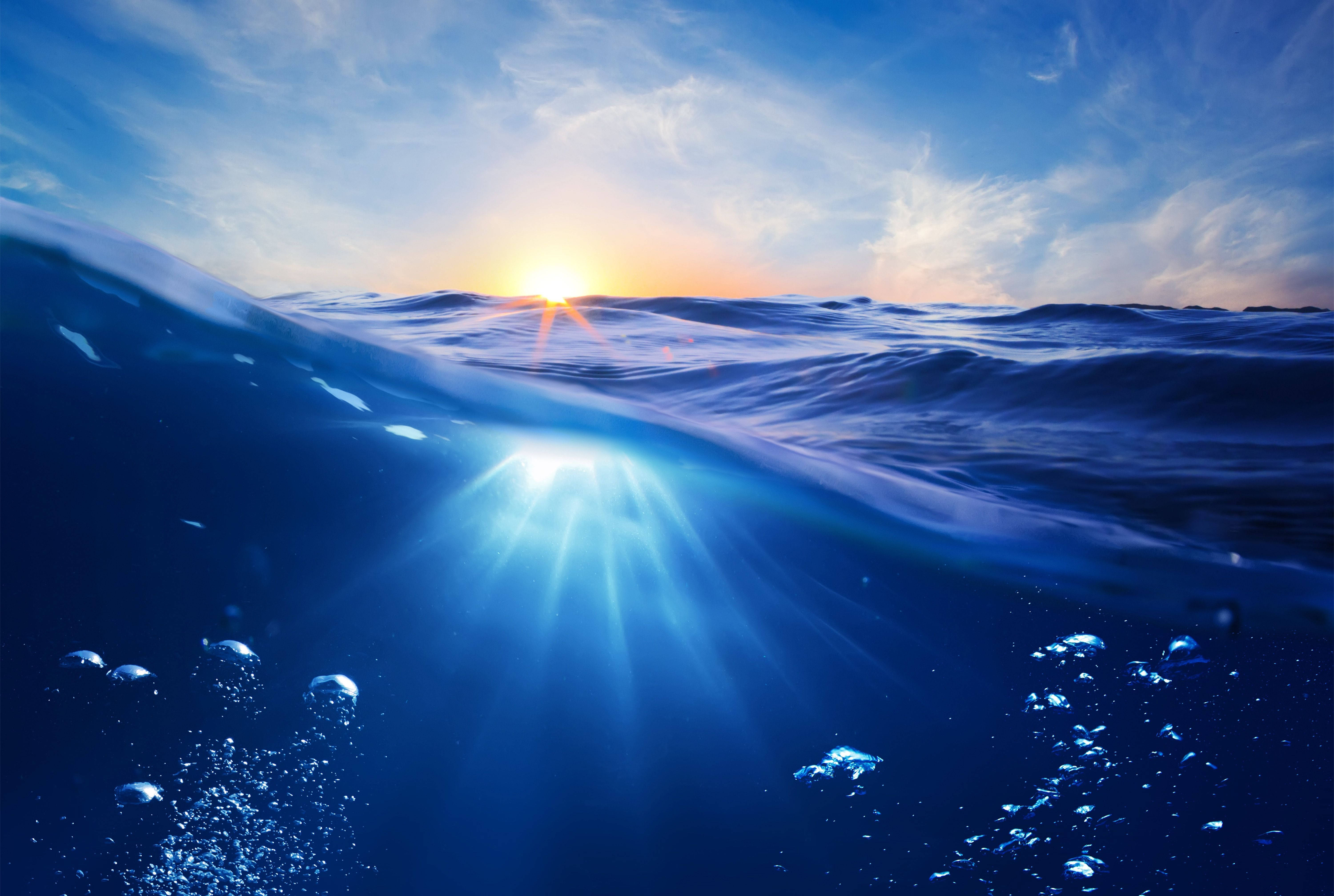 4K 桌布 壁紙 — 夕陽從上方穿透海浪，氣泡在深藍色海水中升起。