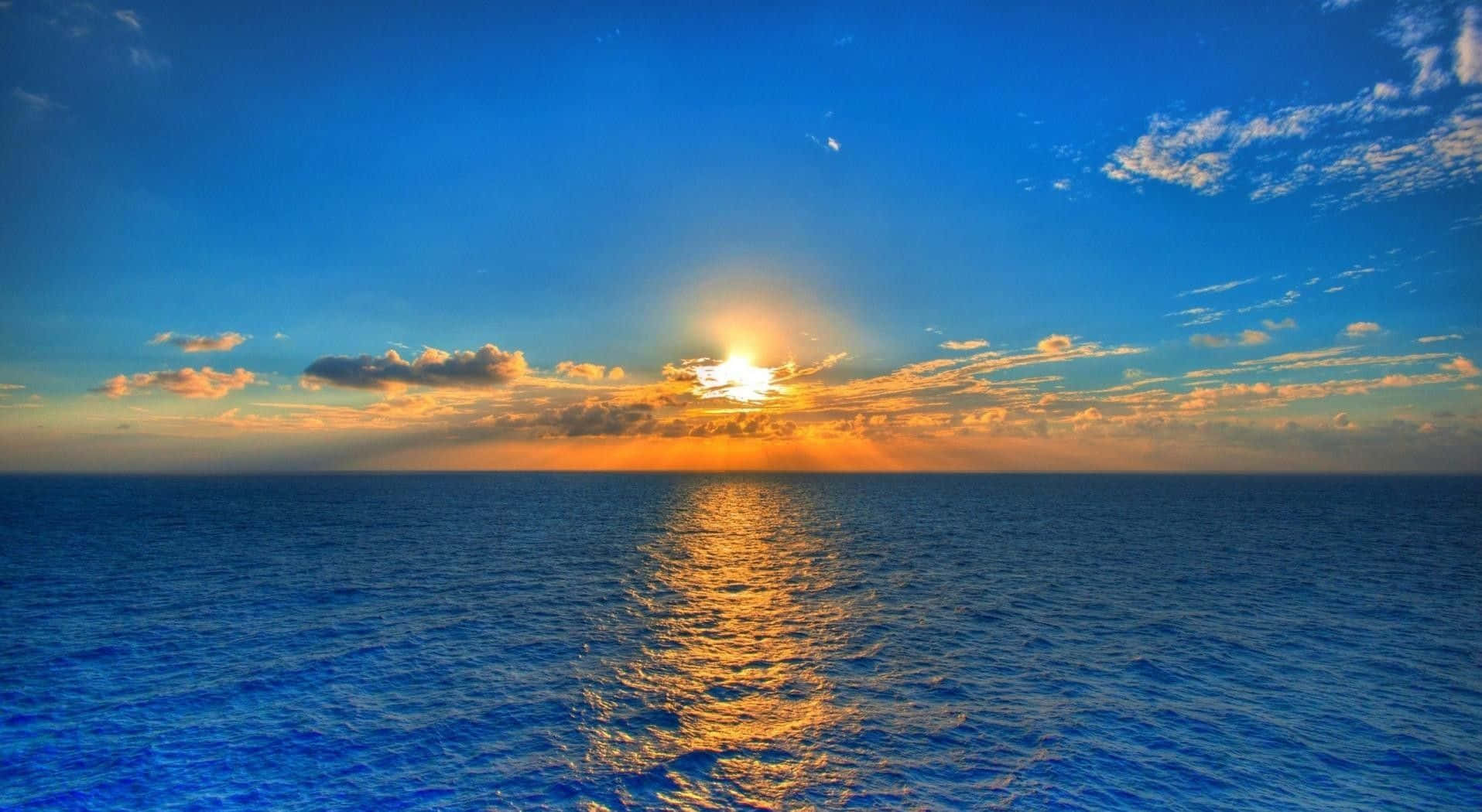 Best Summer 桌布 壁紙 — 夕陽映照海洋，金色光線穿過雲層，反射在深藍色的水面上。