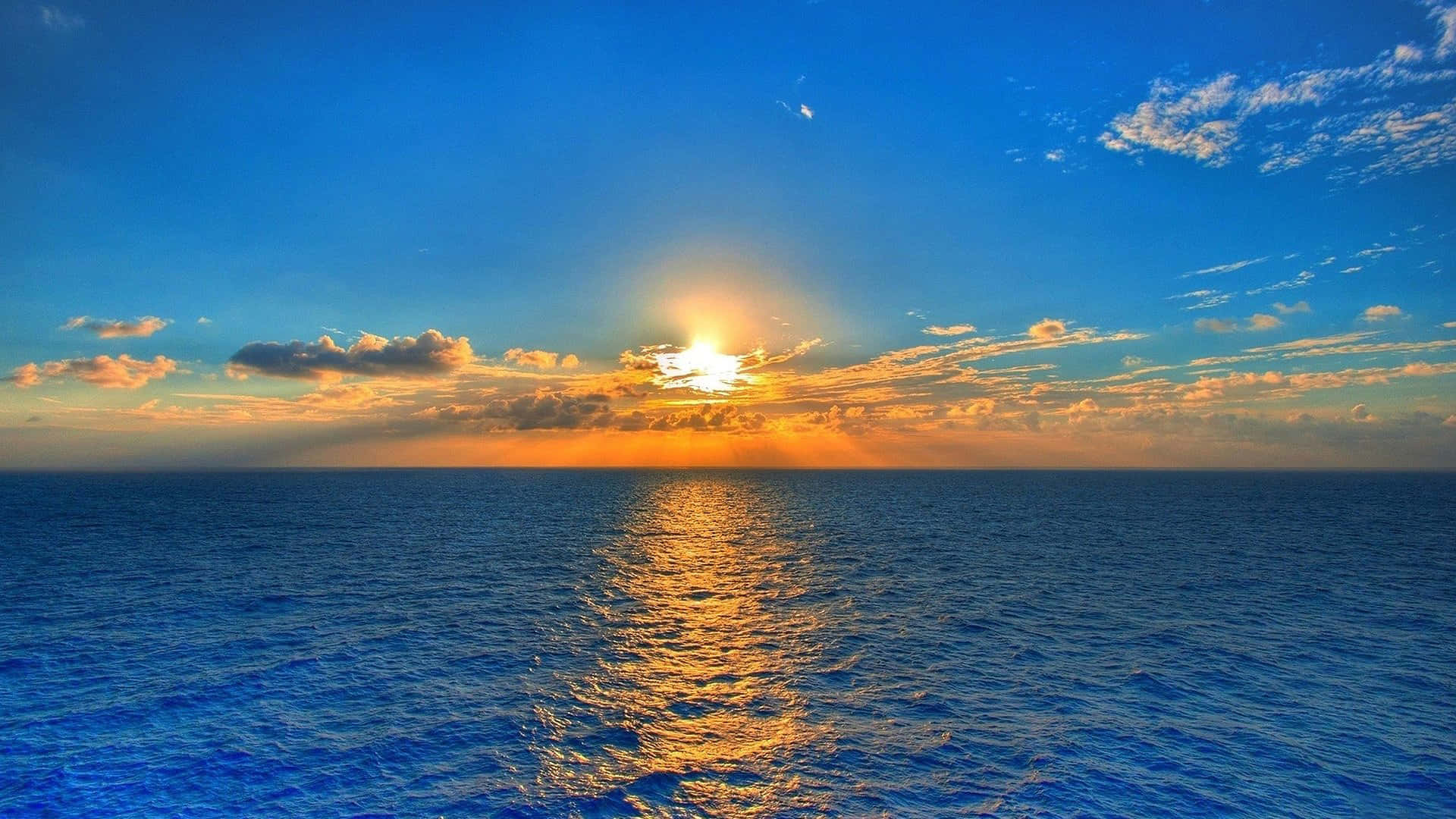 桌布 壁紙 — 夕陽映照海洋，金色光芒在波光粼粼的藍色水面上反射，天空色彩斑斕。