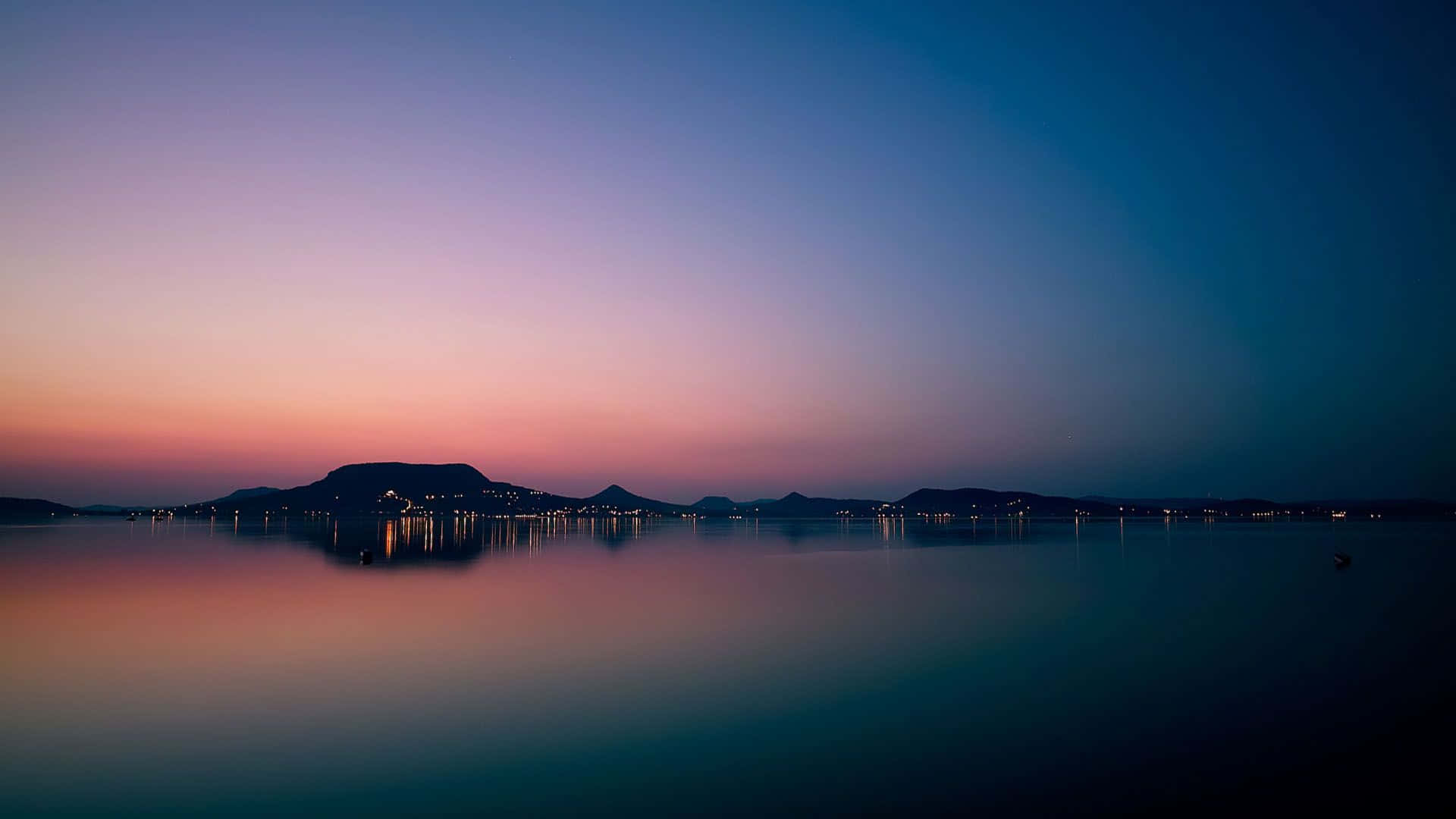 夕陽映照湖面，遠山為背景的景色 壁紙