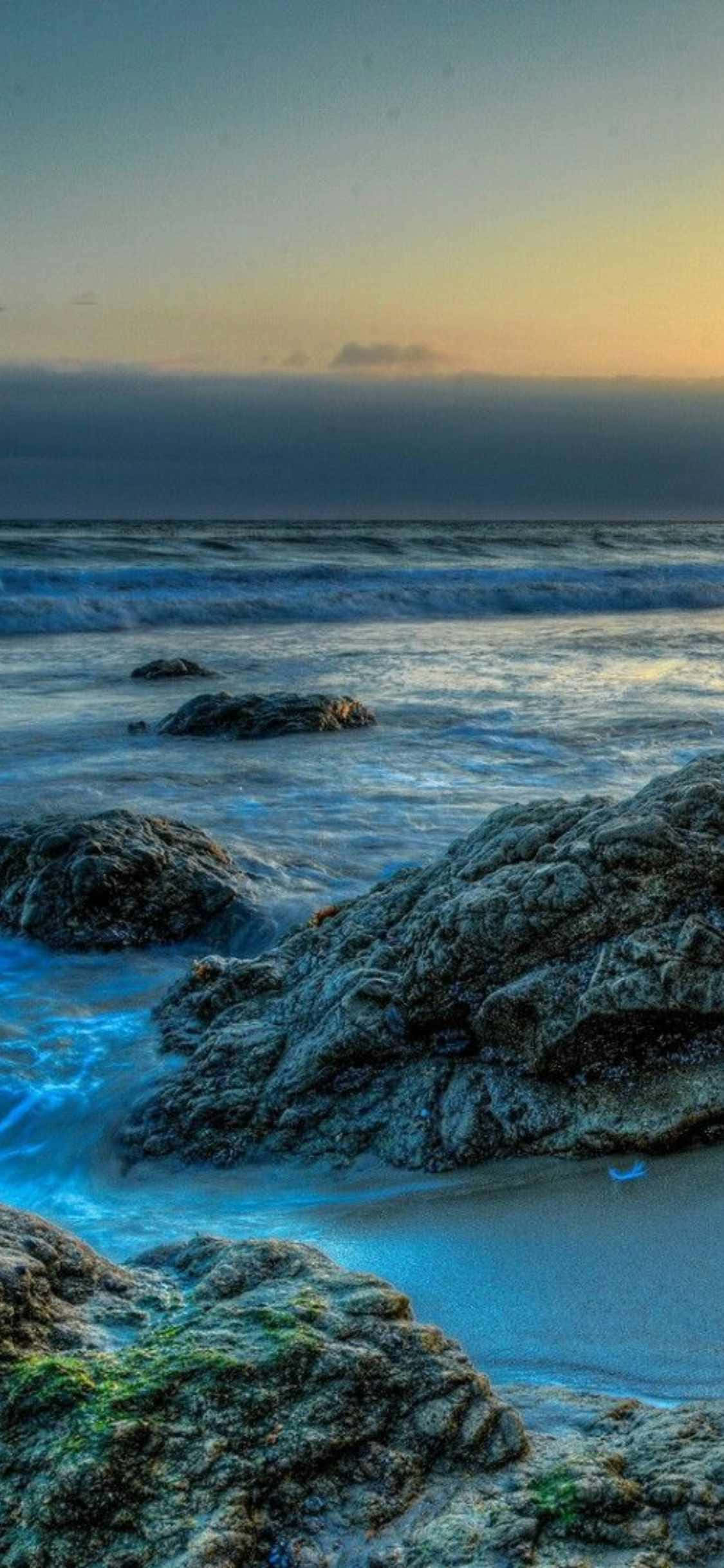 夕陽時分，沙灘上的岩石與海水 壁紙