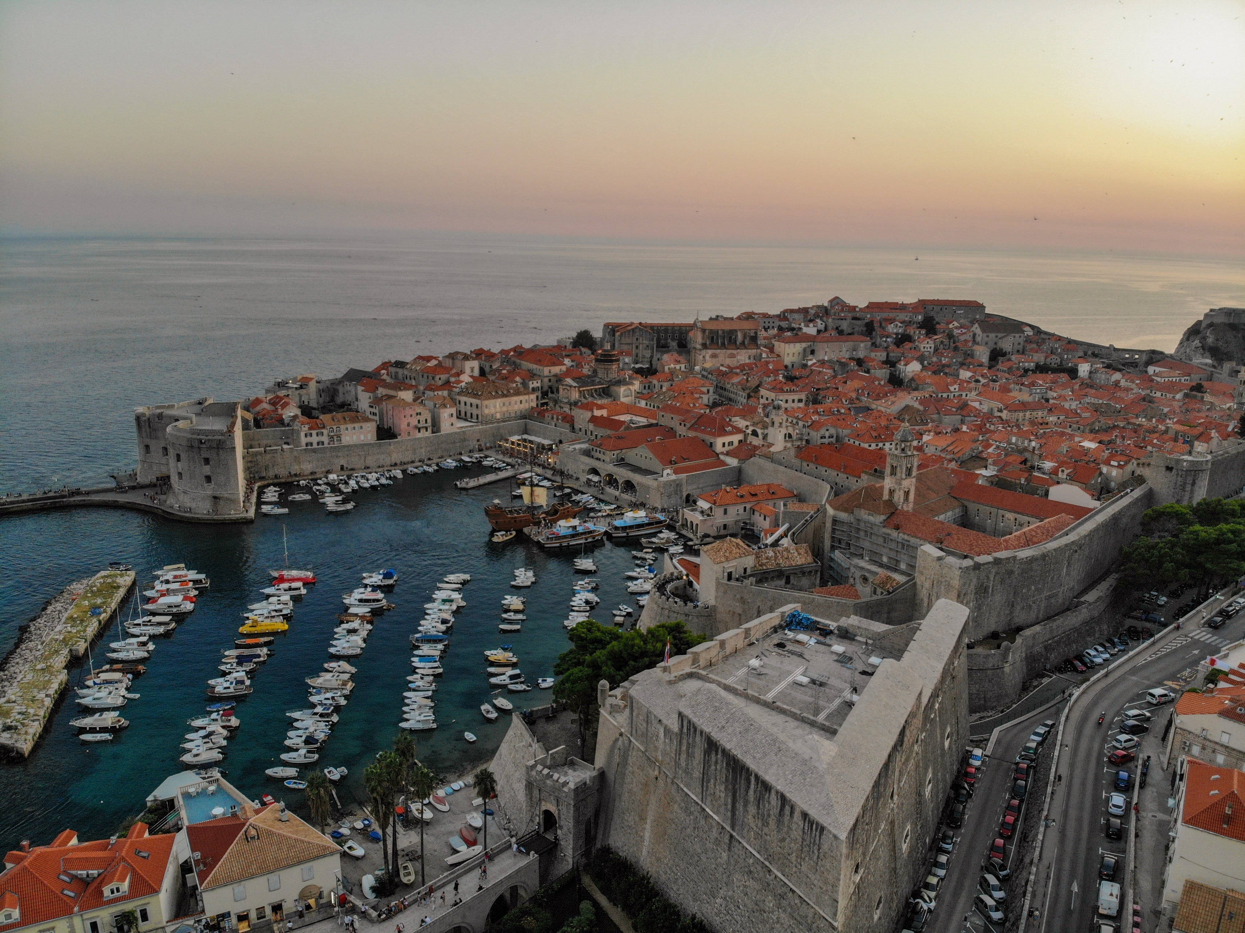 Croatia 桌布 壁紙 — 夕陽沐浴在杜布羅夫尼克的古老石牆和陶土屋頂上，下方的港口點綴著船隻。