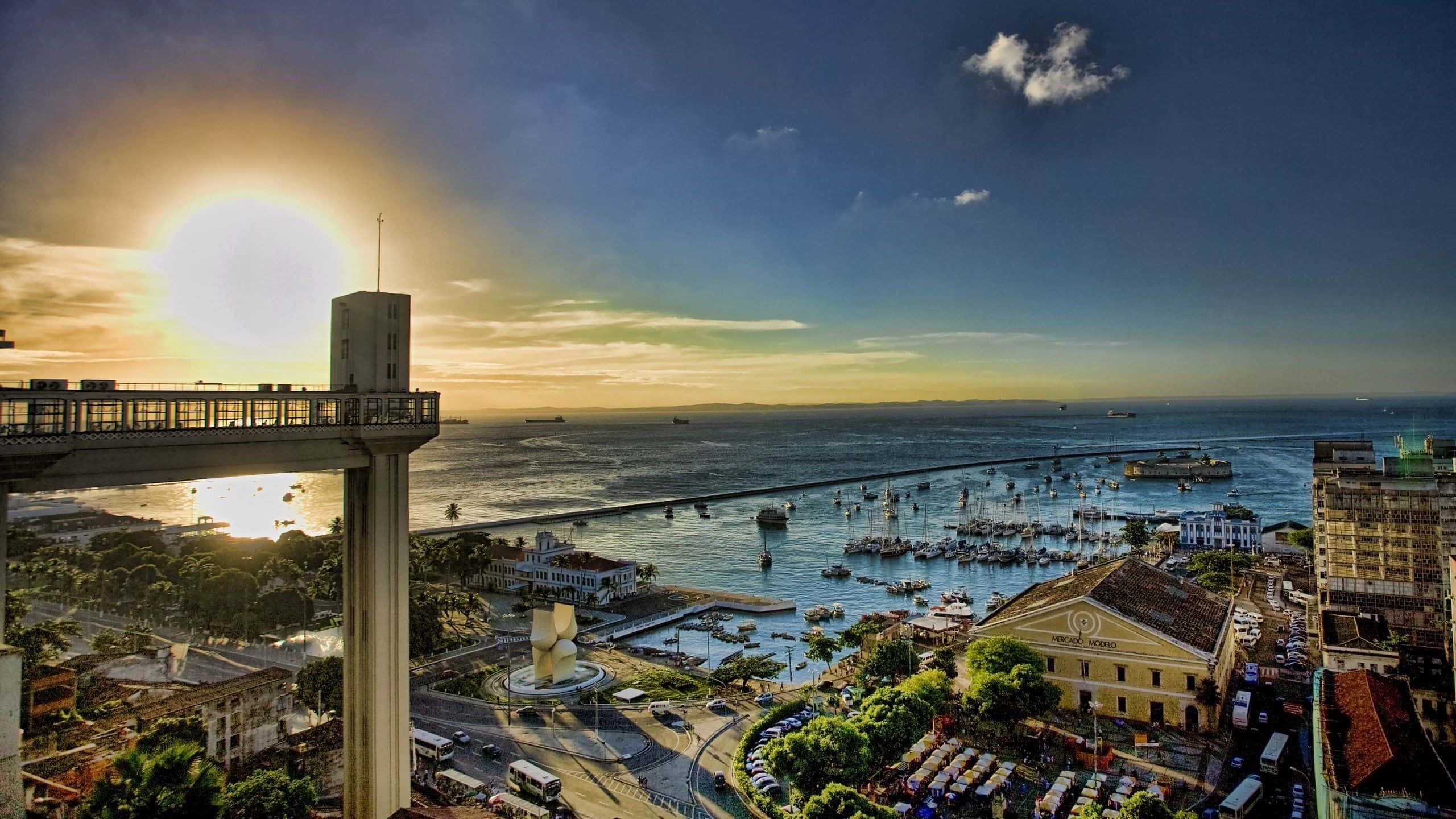 巴西 桌布 壁紙 — 夕陽沐浴著繁華的海岸城市景觀，高聳的橋樑、港口的船隻和歷史建築在溫暖的金色光芒下。