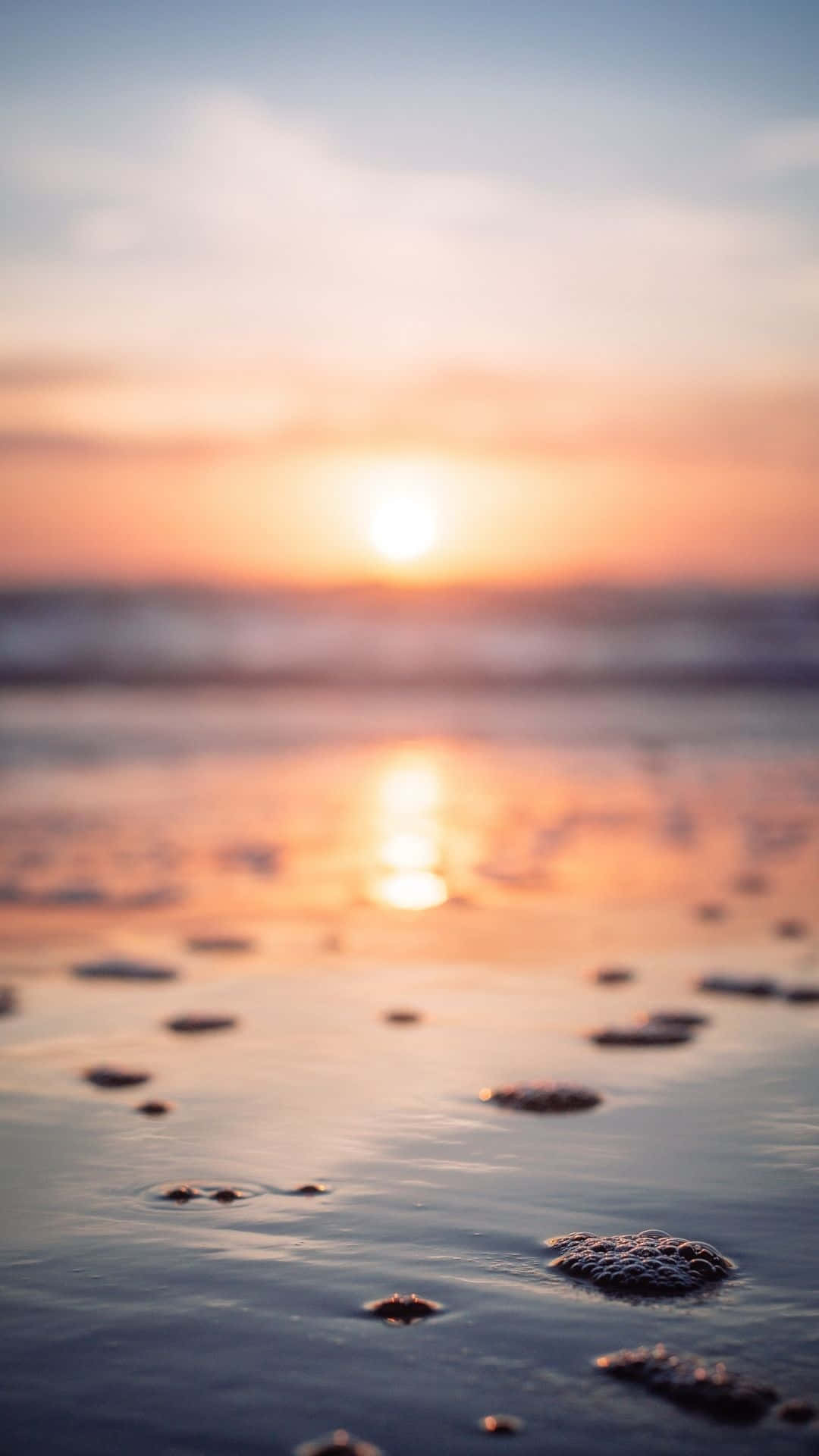 寧靜美學 桌布 壁紙 — 夕陽溫暖地照耀在海浪上，前景有淺水和散落的泡沫。