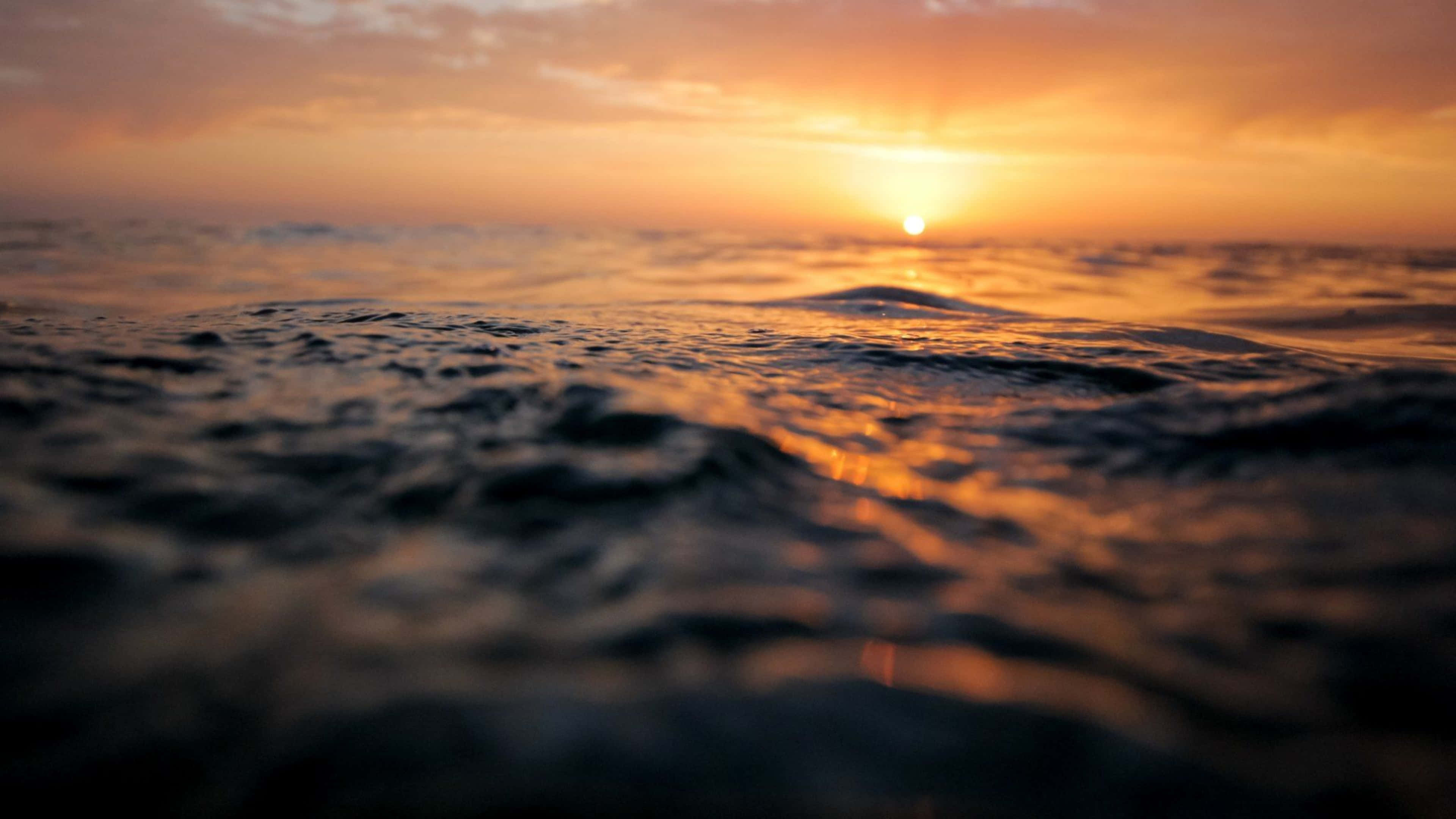 Ocean Blue 桌布 壁紙 — 夕陽溫暖地照耀在海浪上，金色的光線反射在紋理豐富的水面上。