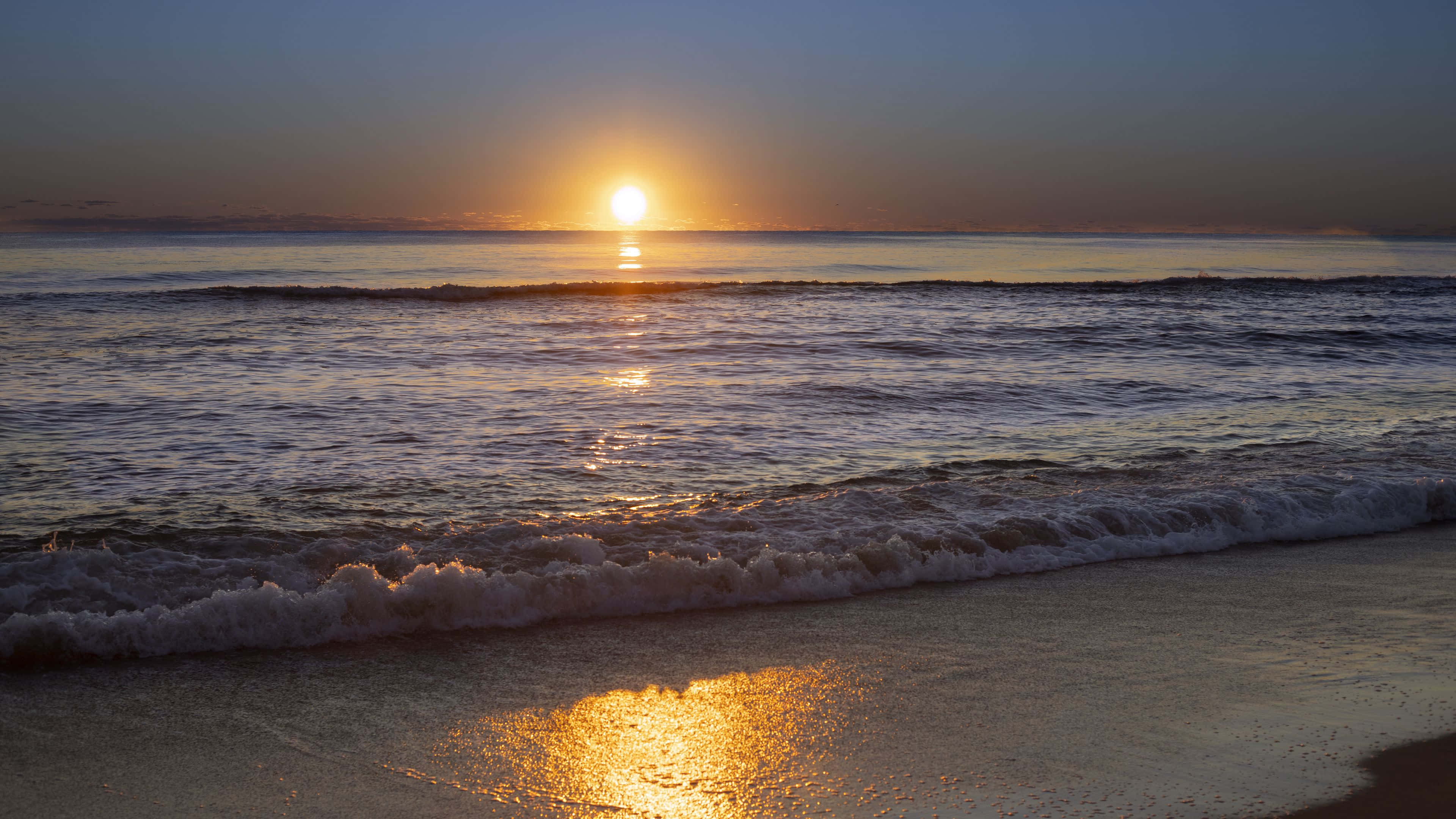 Horizon 桌布 壁紙 — 夕陽溫暖地照耀著海洋波浪，波浪滾滾湧上沙灘，金色倒影在濕沙上閃爍。