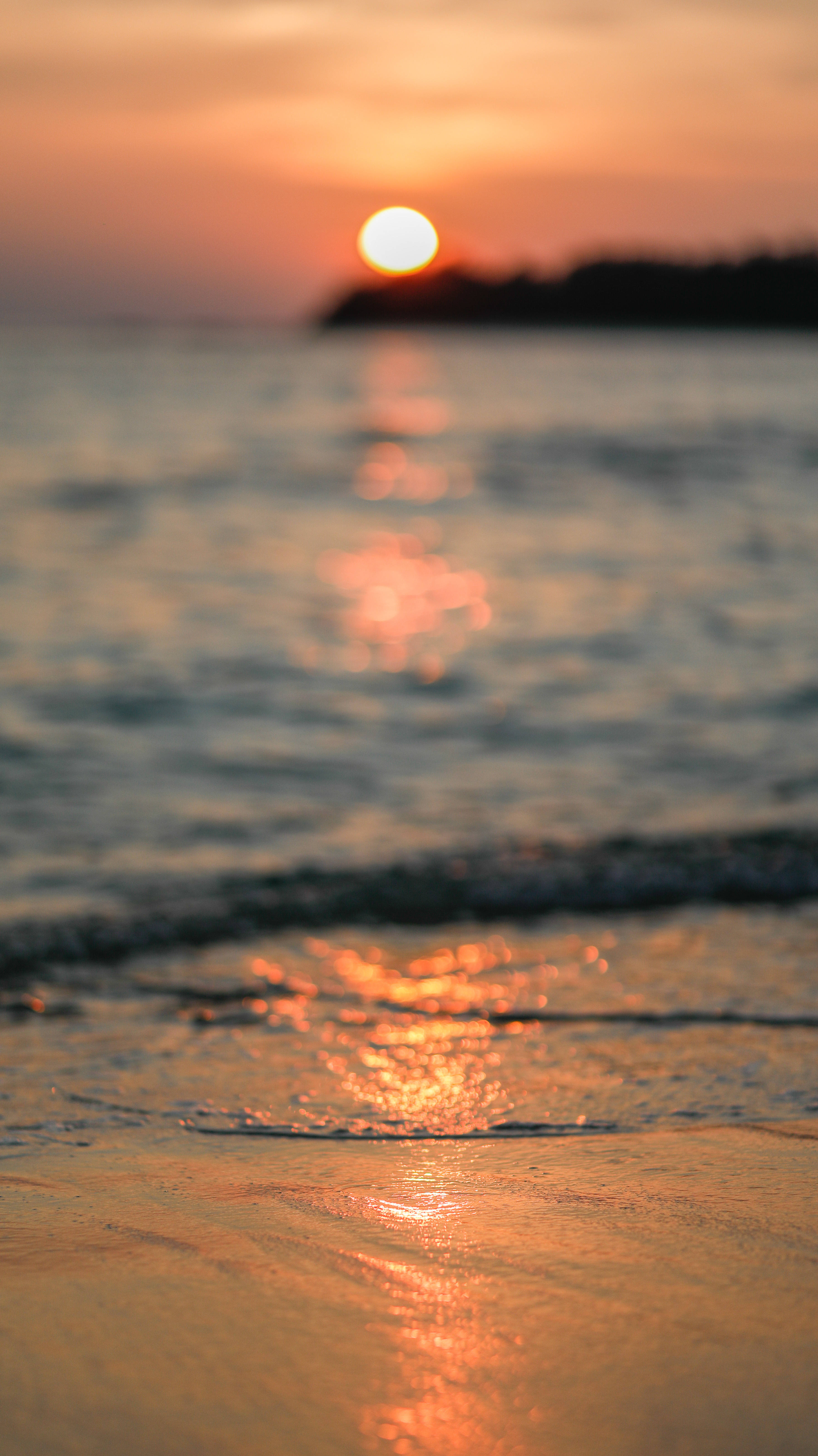 Amazing 桌布 壁紙 — 夕陽溫暖地照耀著海浪拍打沙灘，遠方陸地輪廓隱約可見。