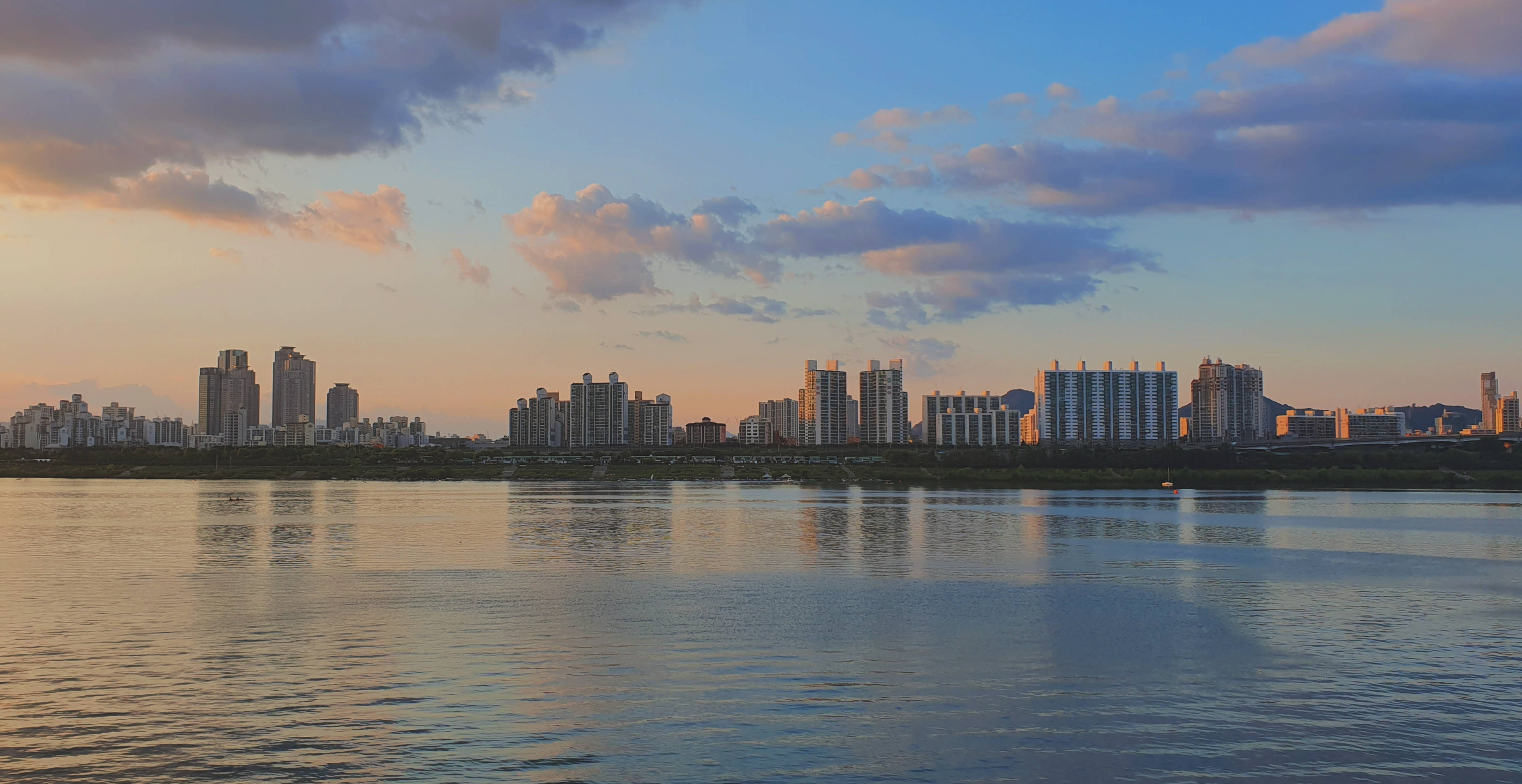 首爾 桌布 壁紙 — 夕陽為城市天際線披上溫暖光輝，倒映在散雲下平靜的河水之中。