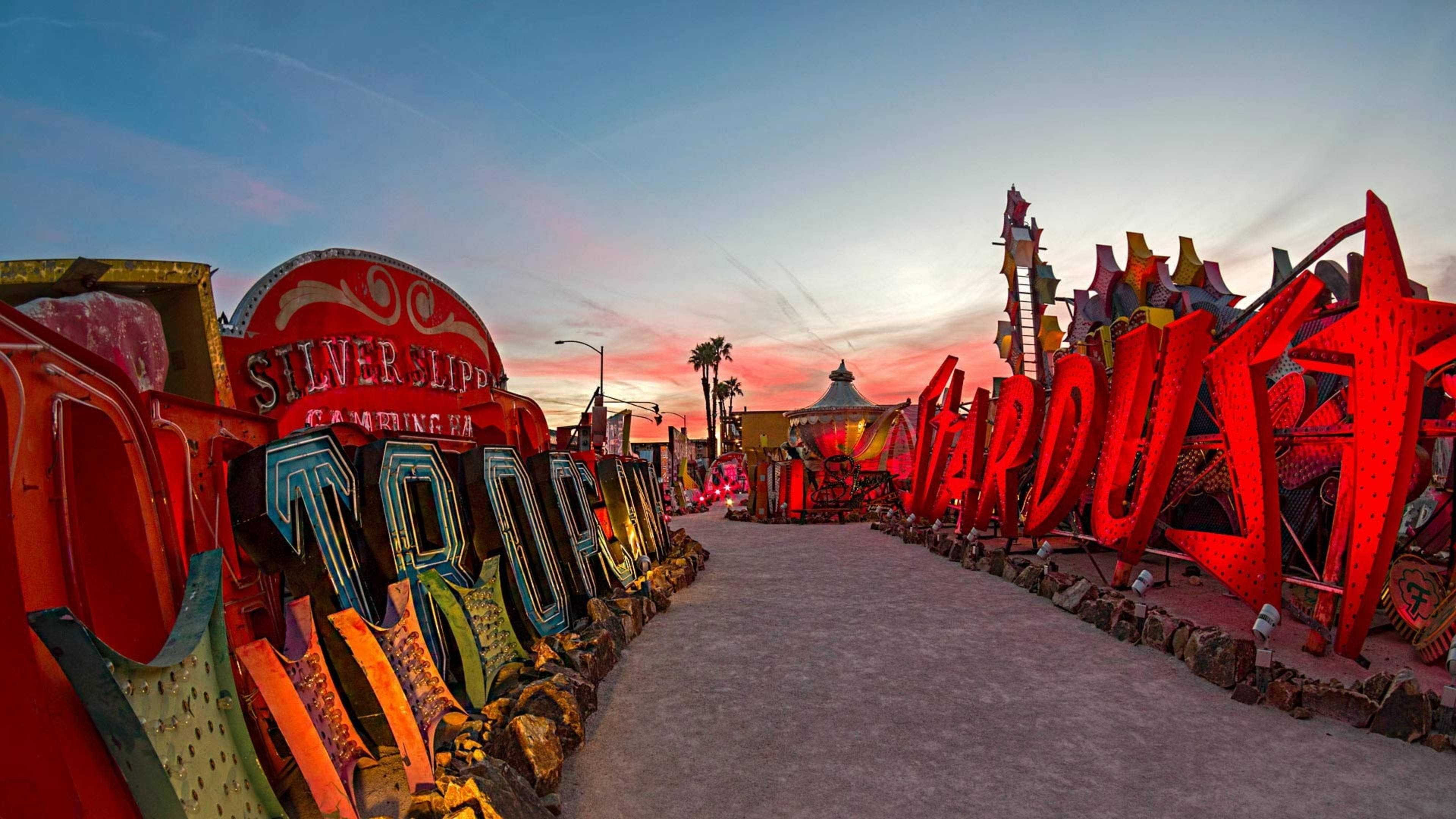 拉斯維加斯 桌布 壁紙 — 夕陽照亮了 Neon Boneyard 一條超現實的沙漠小徑，兩旁擺放著超大型、色彩繽紛的復古賭場招牌。