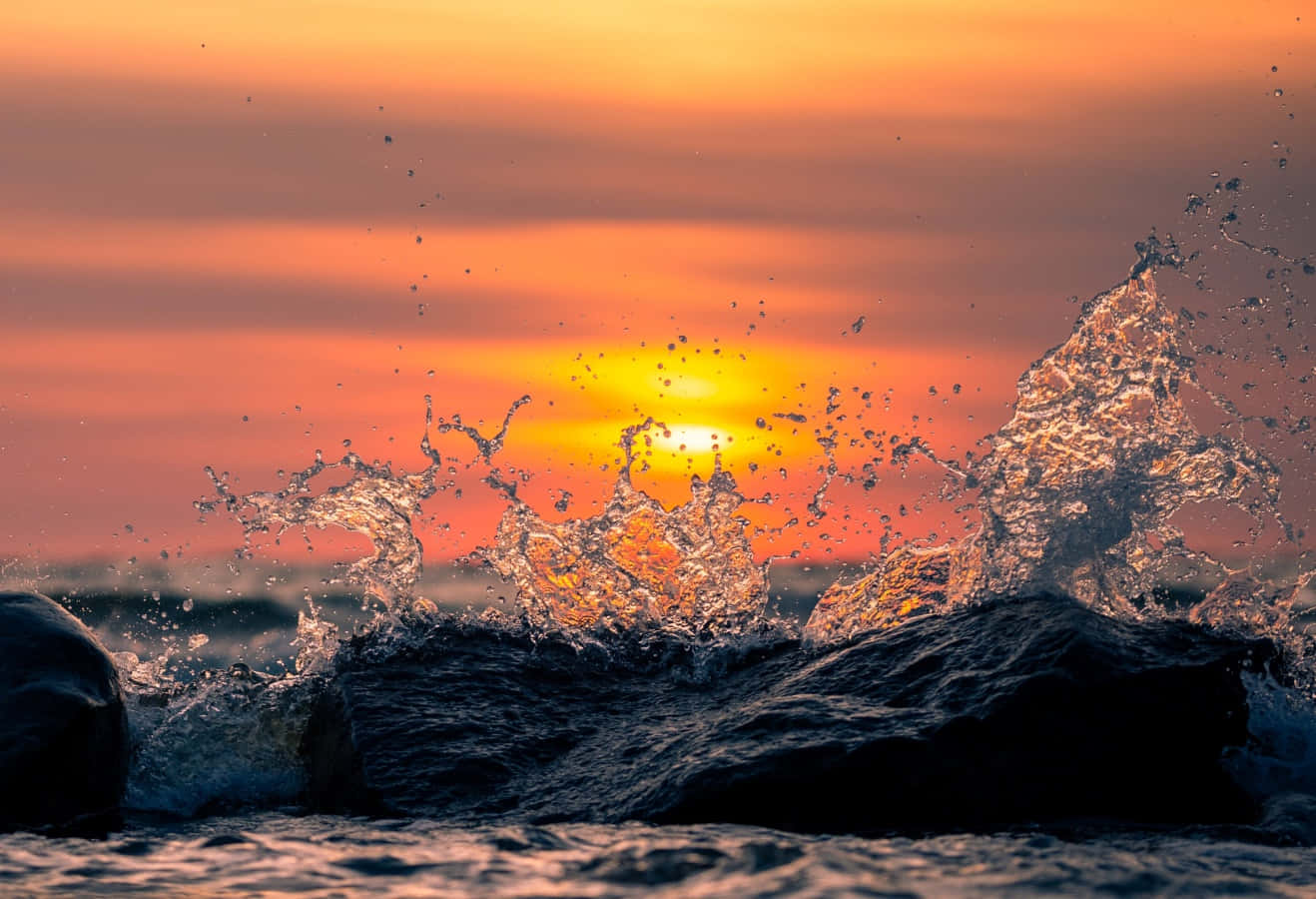 Splash 桌布 壁紙 — 夕陽照亮了撞擊在暗色岩石上的海浪，呈現出鮮豔的橙色和金色色調。