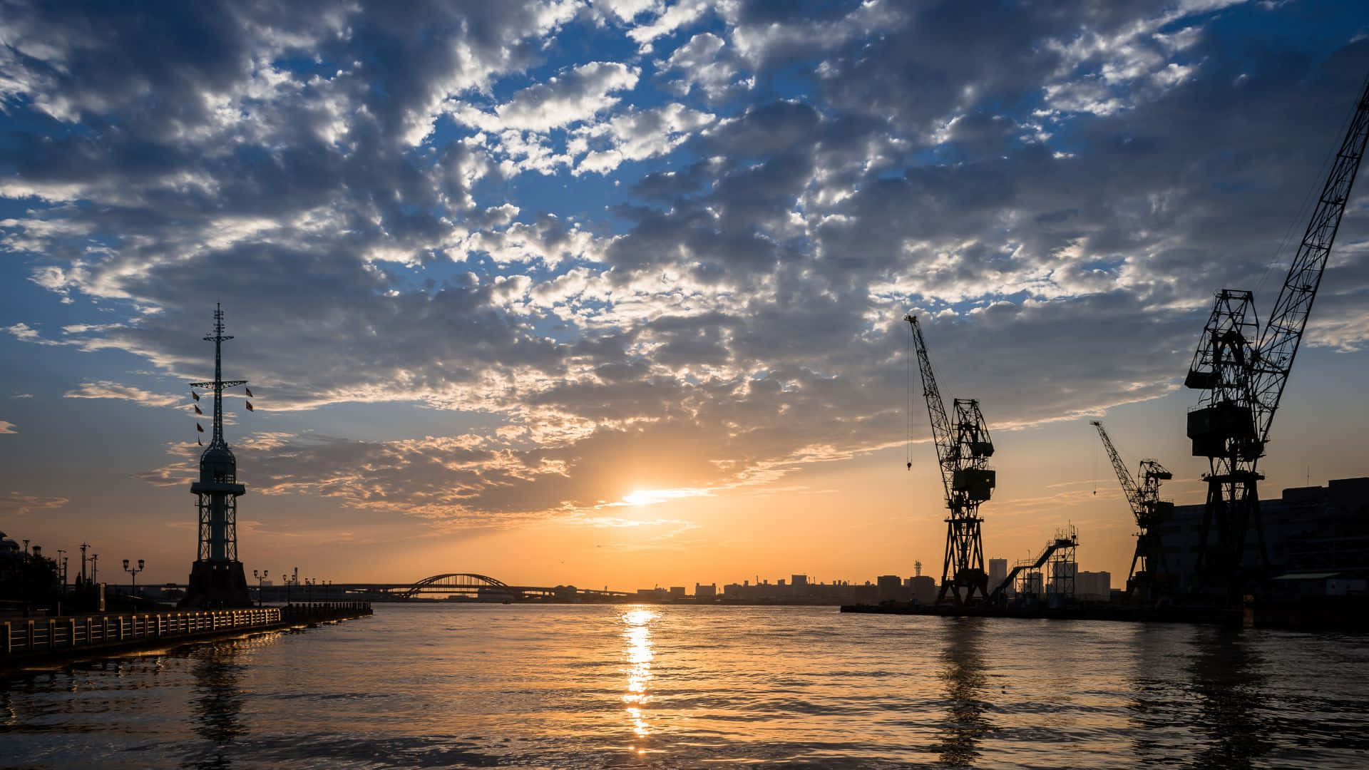 日出 桌布 壁紙 — 夕陽照耀著港口，起重機和燈塔在戲劇性的雲層中形成剪影。